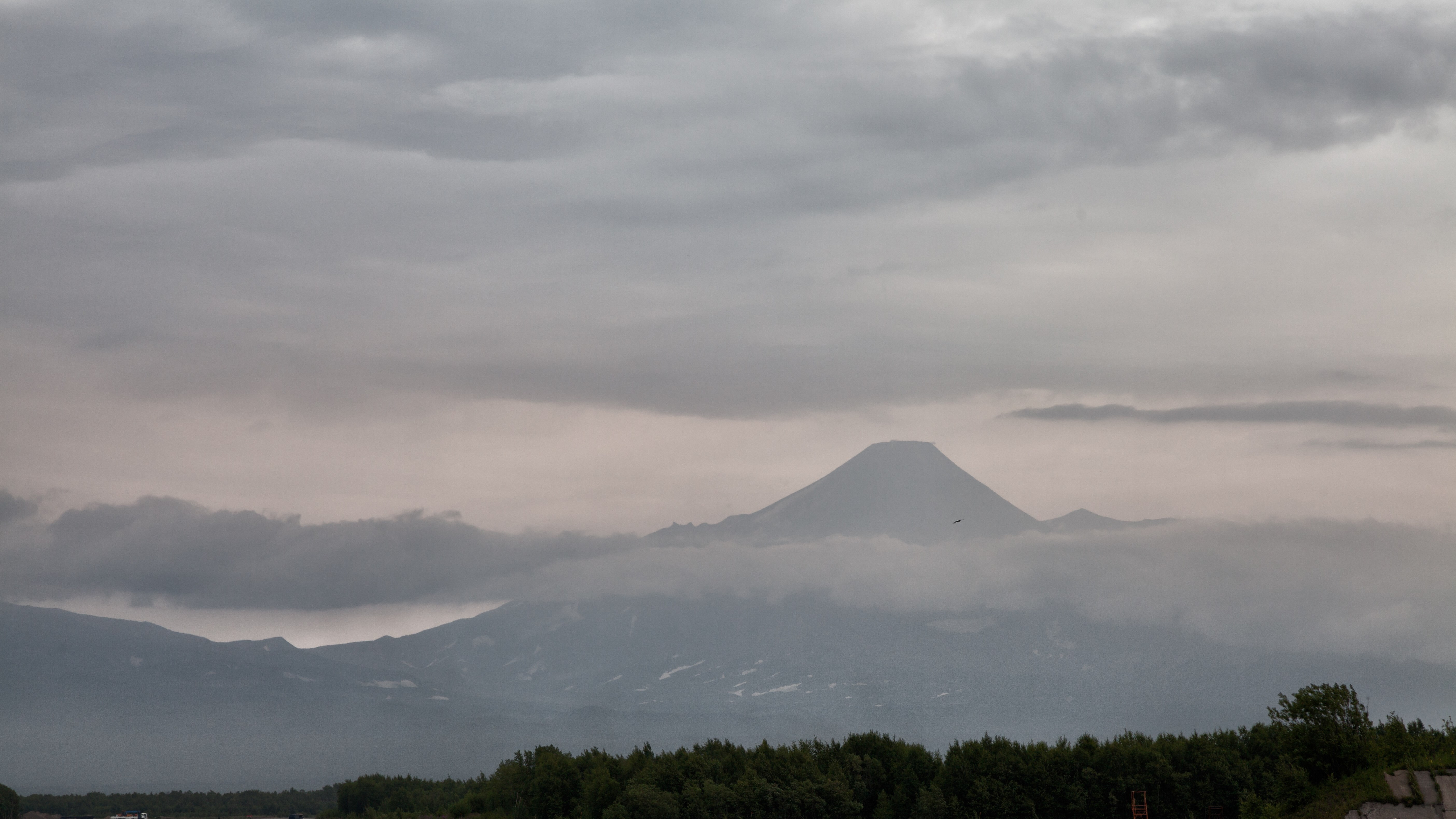 Volcano peak shrouded in clouds with a forest in the foreground HD Wallpaper