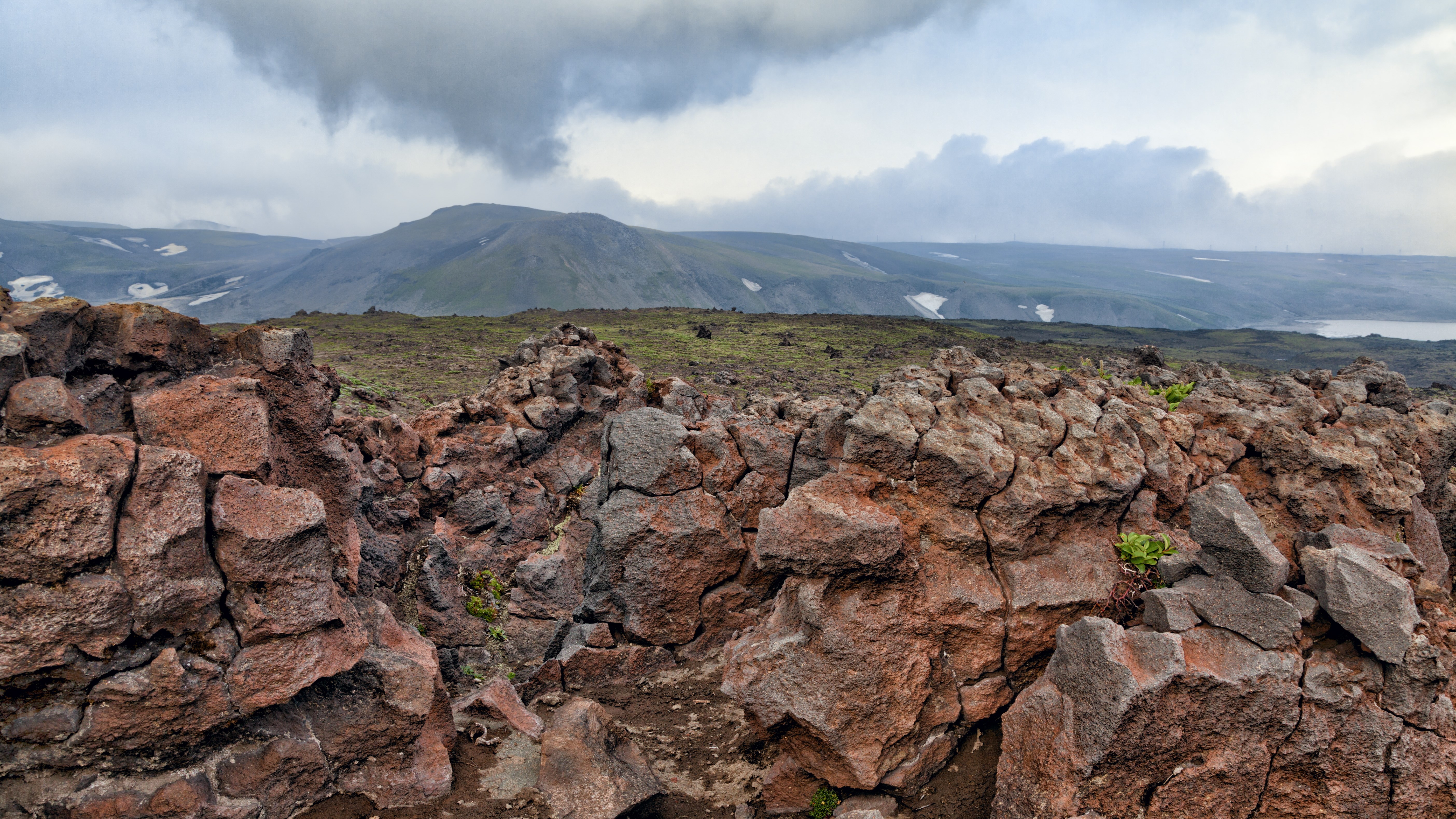Rocky volcanic landscape with distant mountains and clouds HD Wallpaper