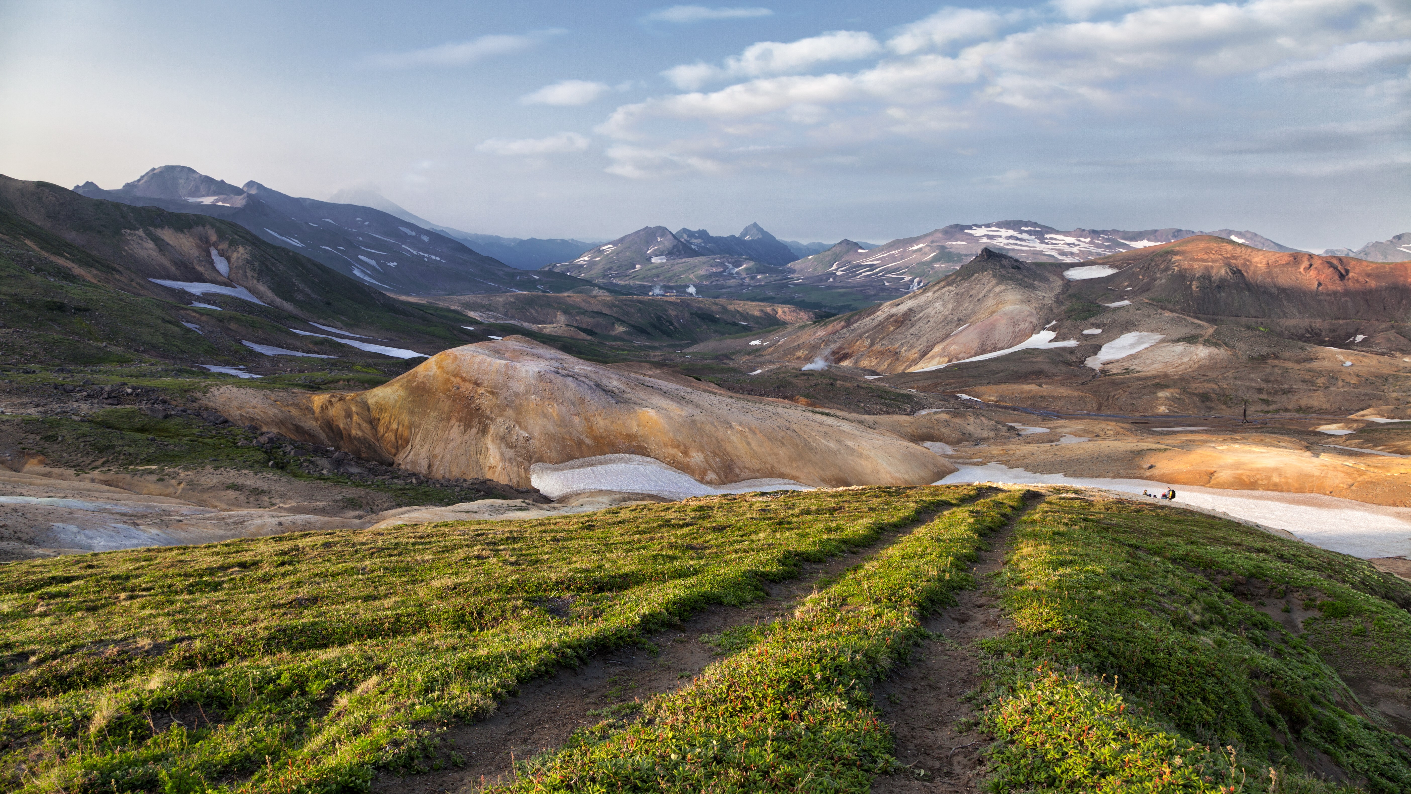 Mountainous landscape with snow patches and a dirt path HD Wallpaper