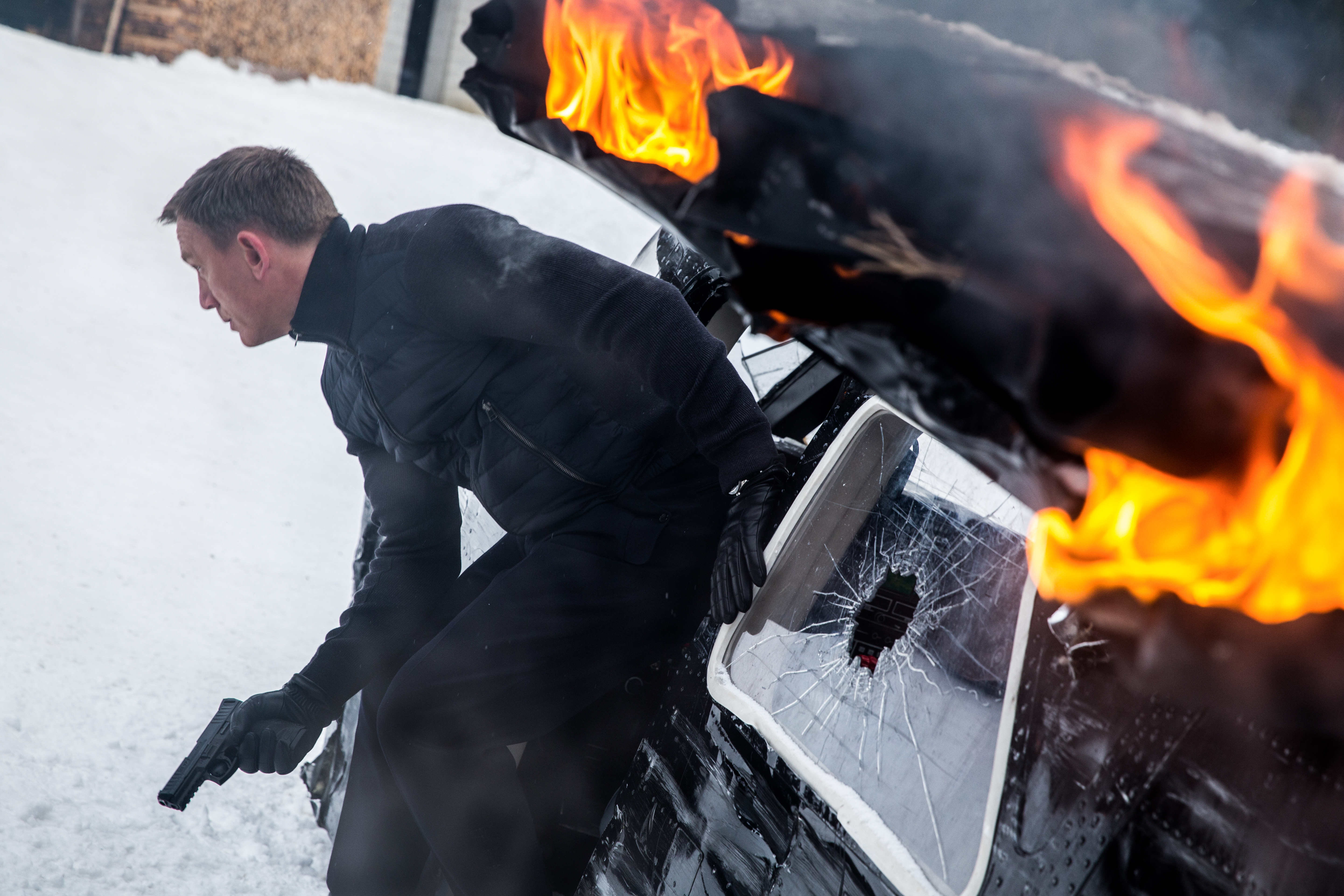 James Bond in a snowy environment with a burning vehicle HD Wallpaper