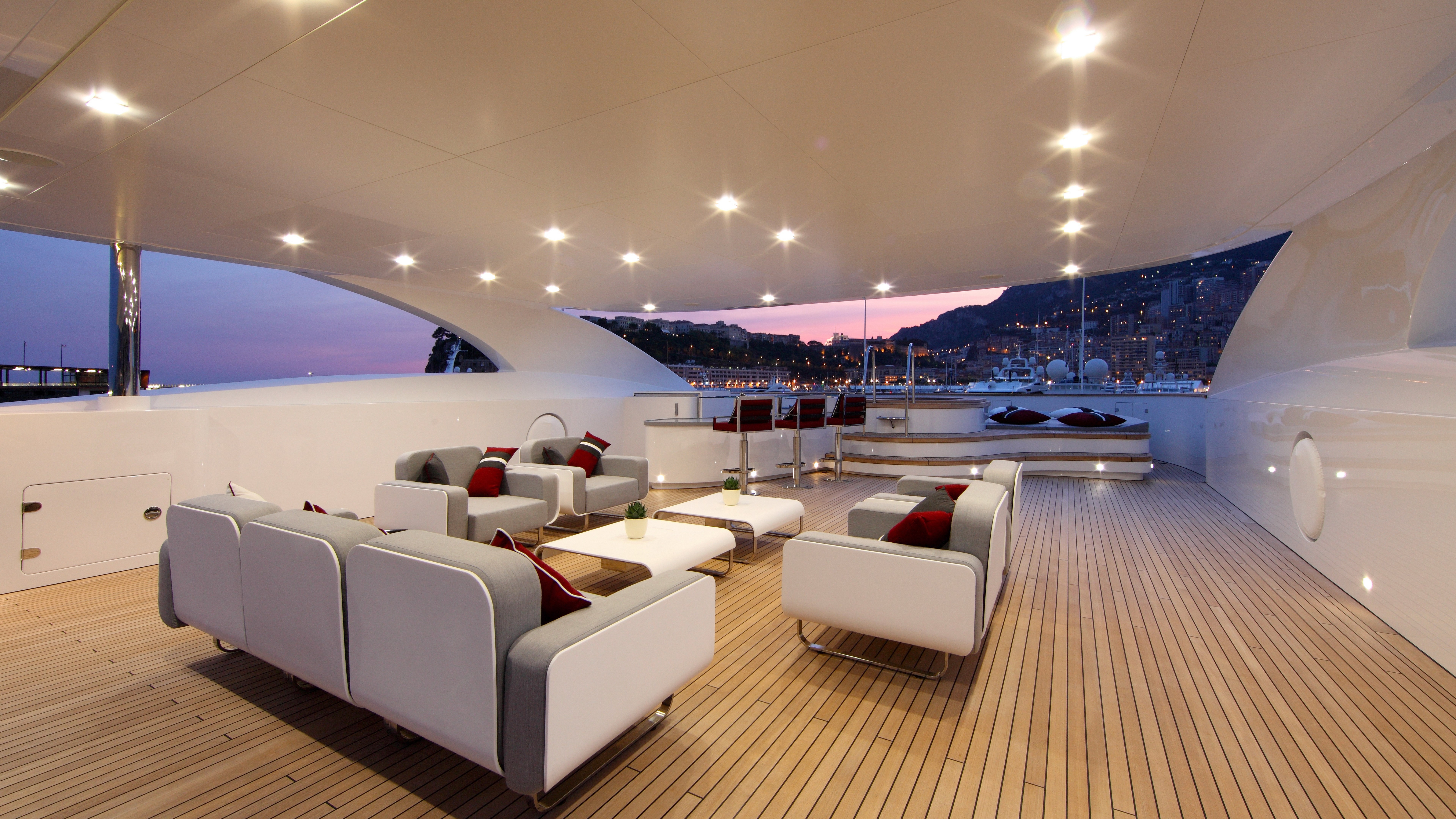 Luxury yacht deck with seating and bar overlooking a harbor at dusk HD Wallpaper