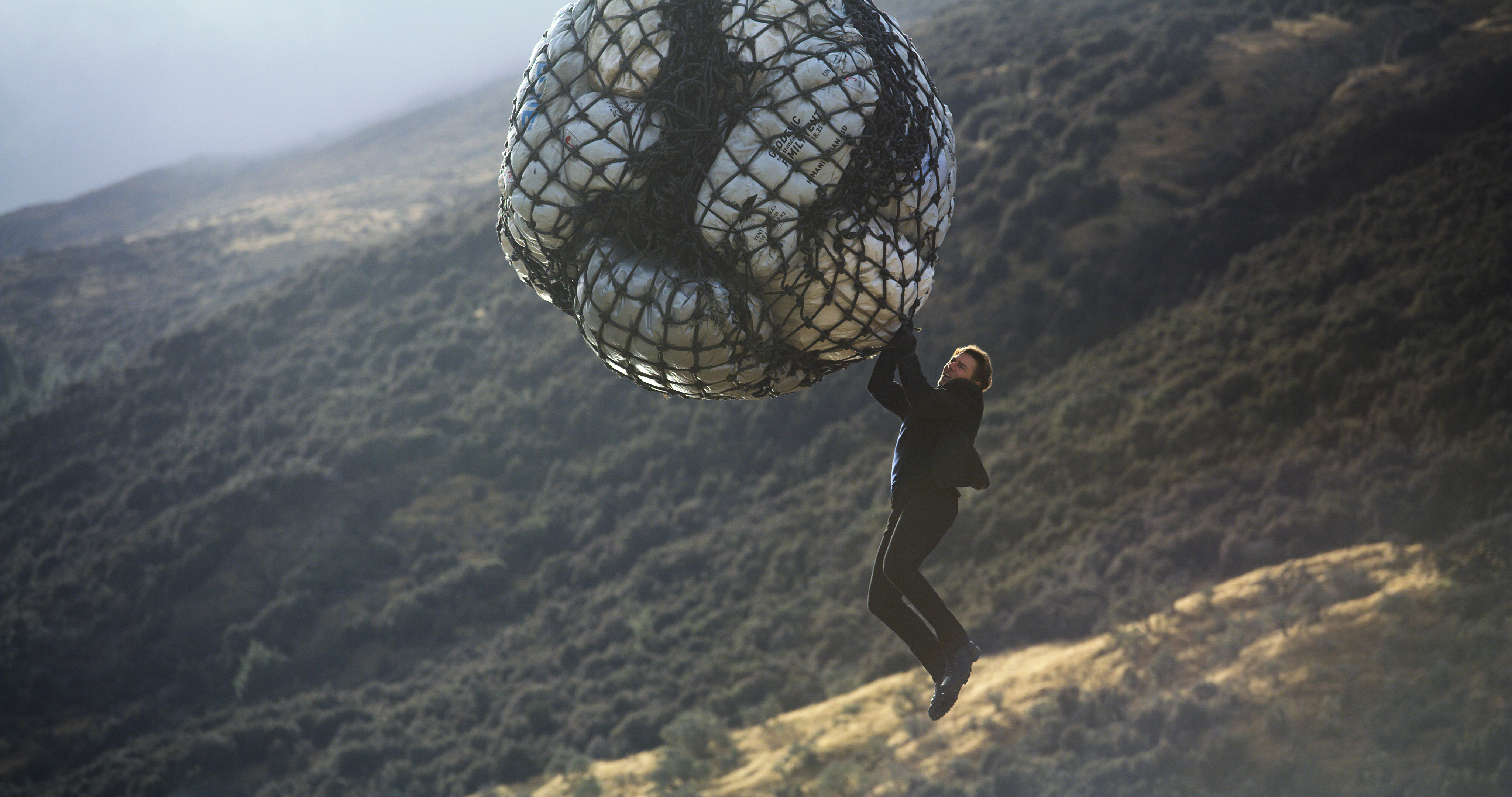 Ethan Hunt hanging from a large net of packages HD Wallpaper