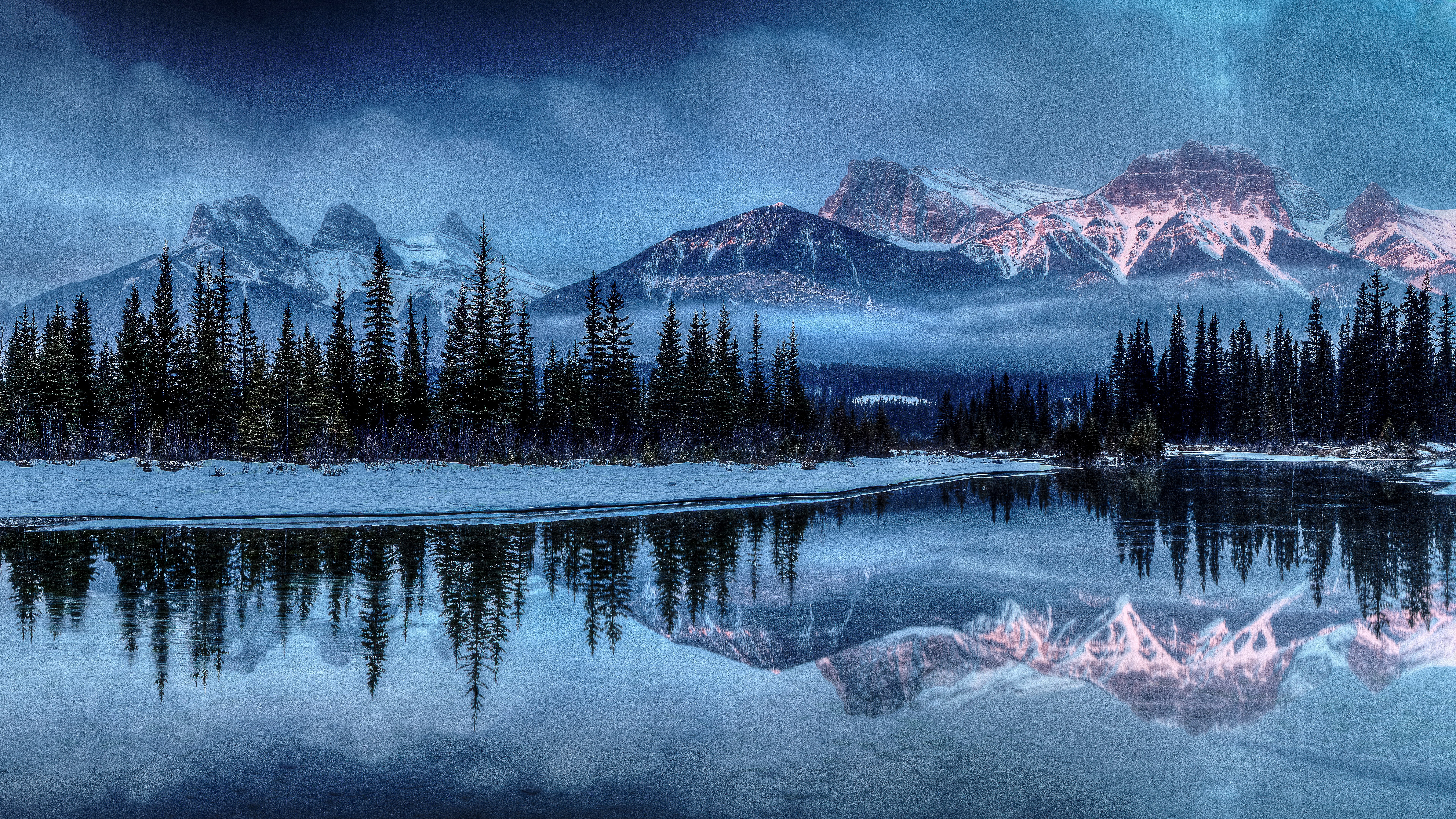 Snowy mountains reflected in a calm lake with pine trees HD Wallpaper