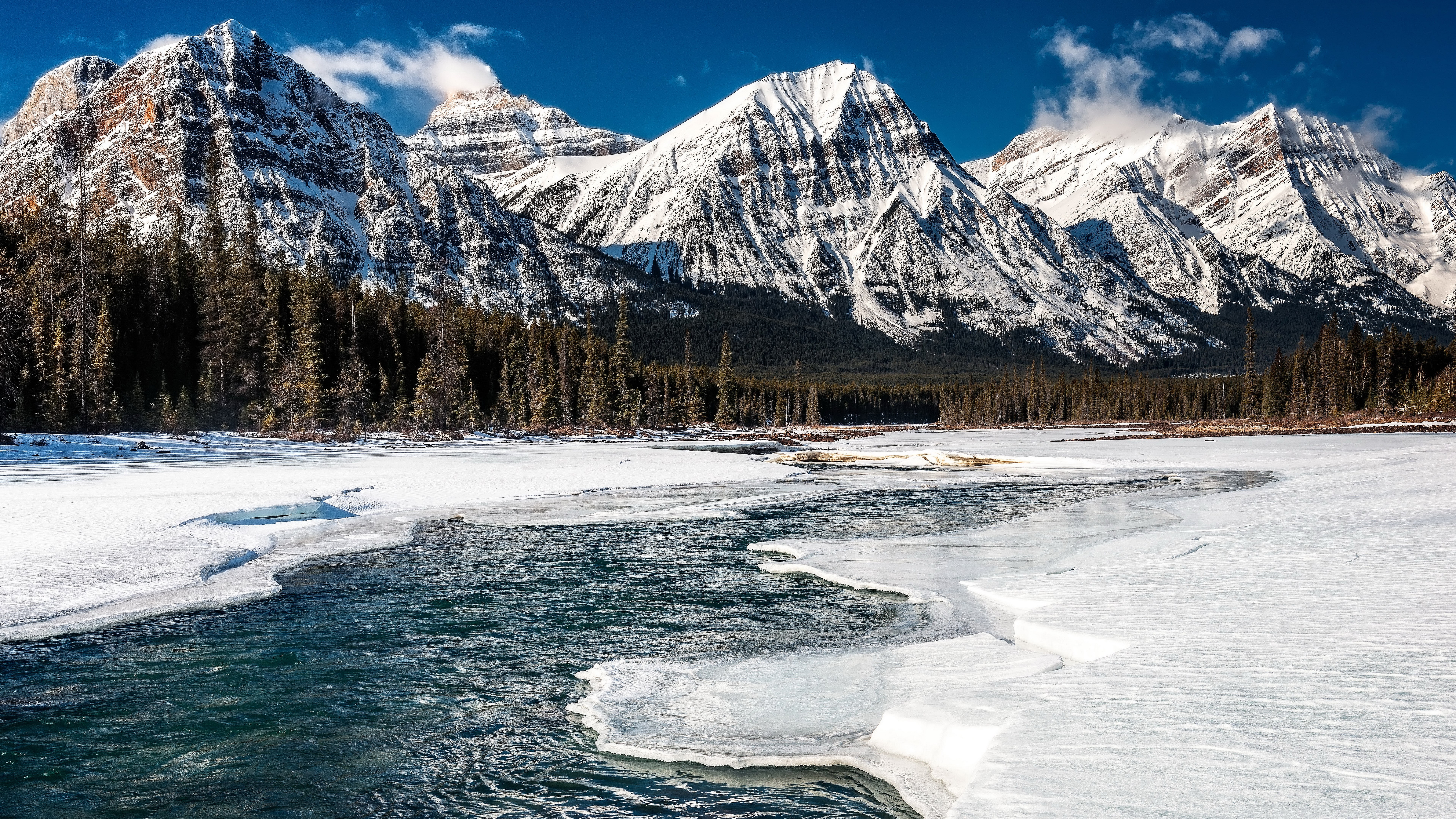 Snowy mountains and a partially frozen river HD Wallpaper