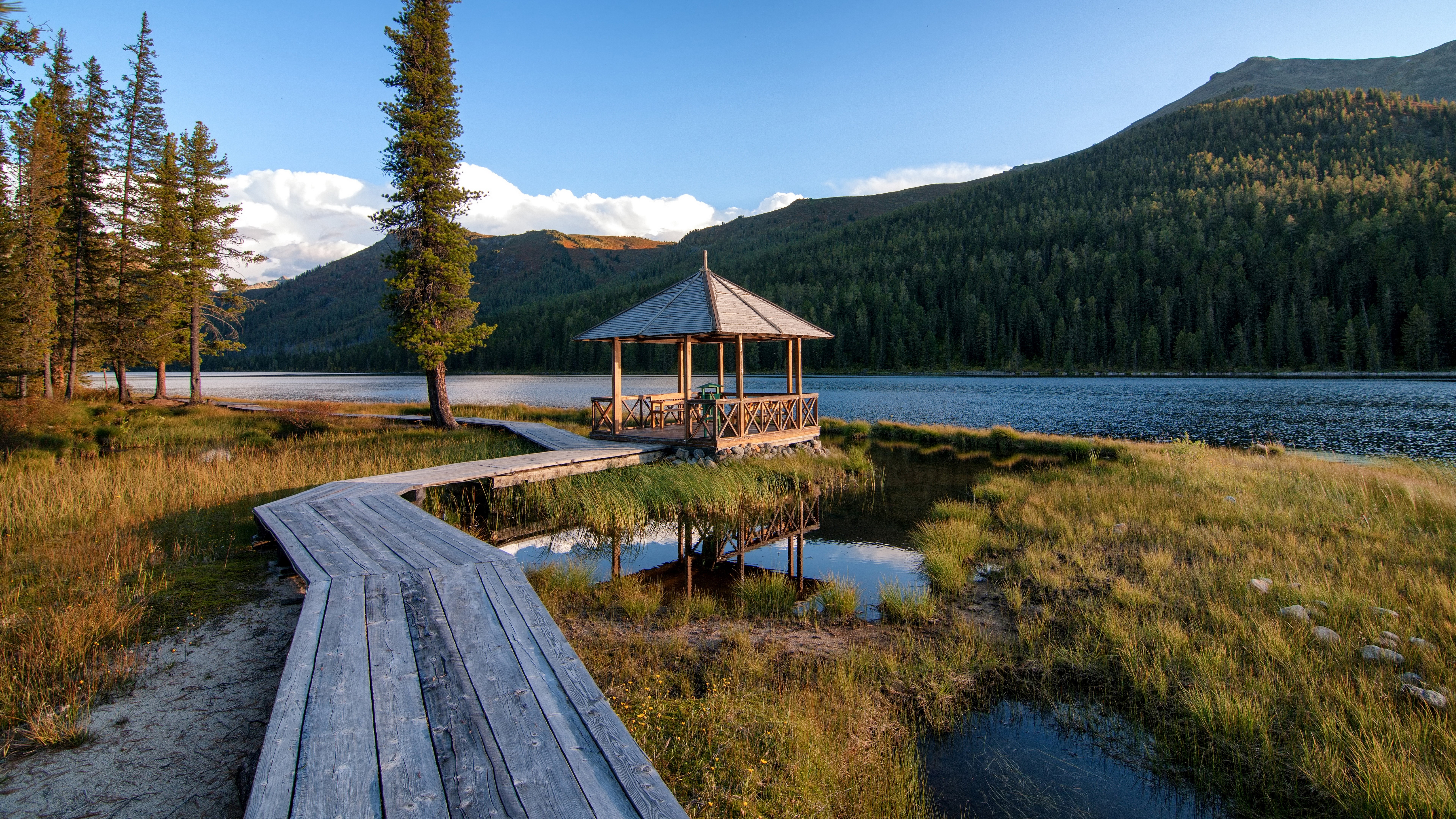 Wooden boardwalk leads to a gazebo by a lake HD Wallpaper