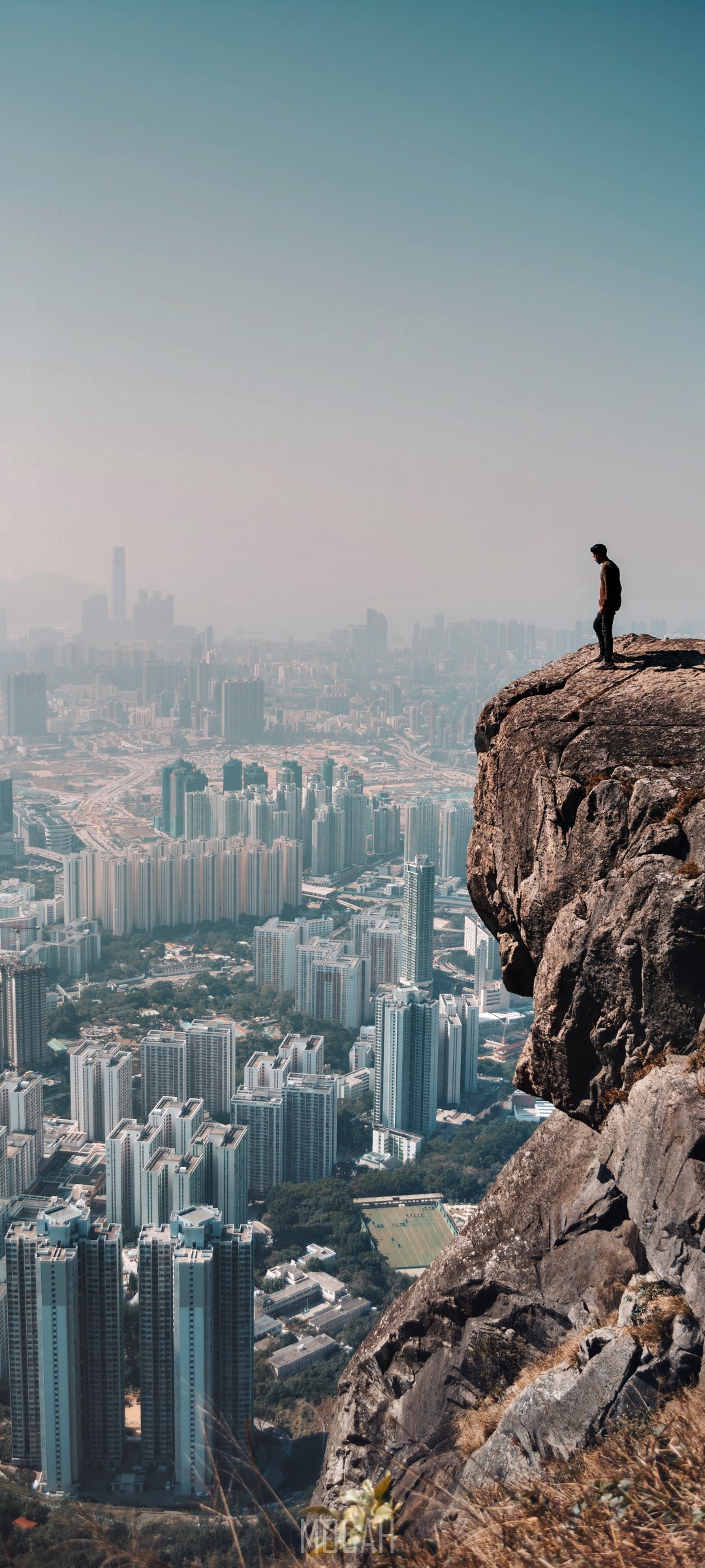 Man standing on a cliff overlooking a city HD Phone Wallpaper