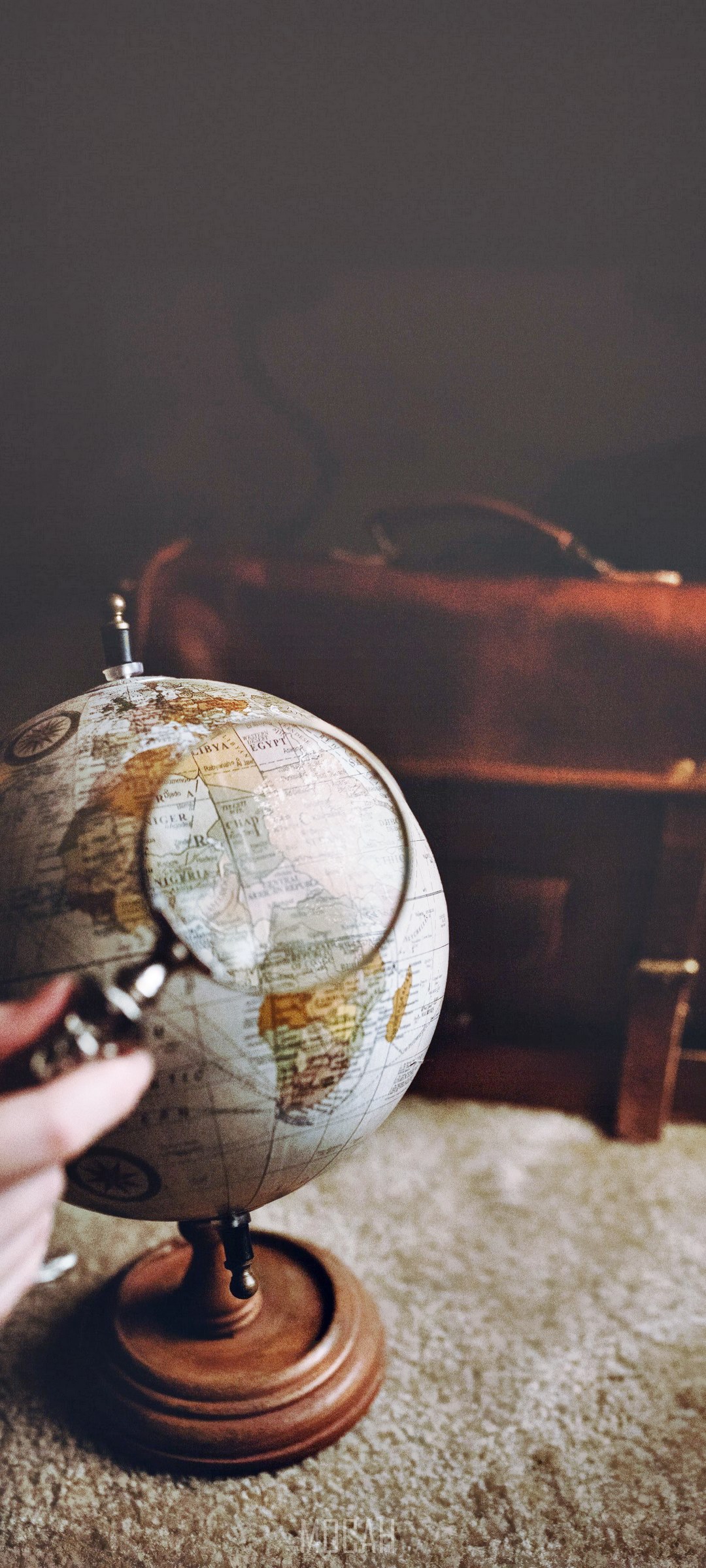 Hand holding magnifying glass over globe with leather bag HD Phone Wallpaper