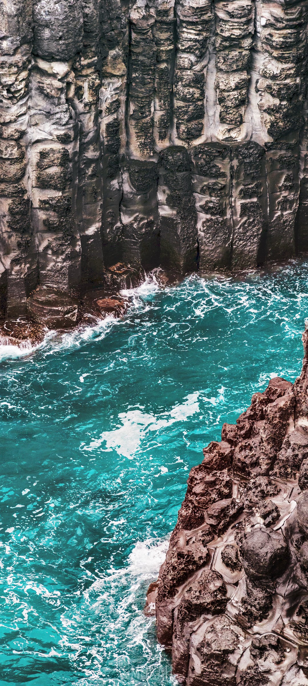 Turquoise water flows between basalt columns on a rocky coast HD Phone Wallpaper