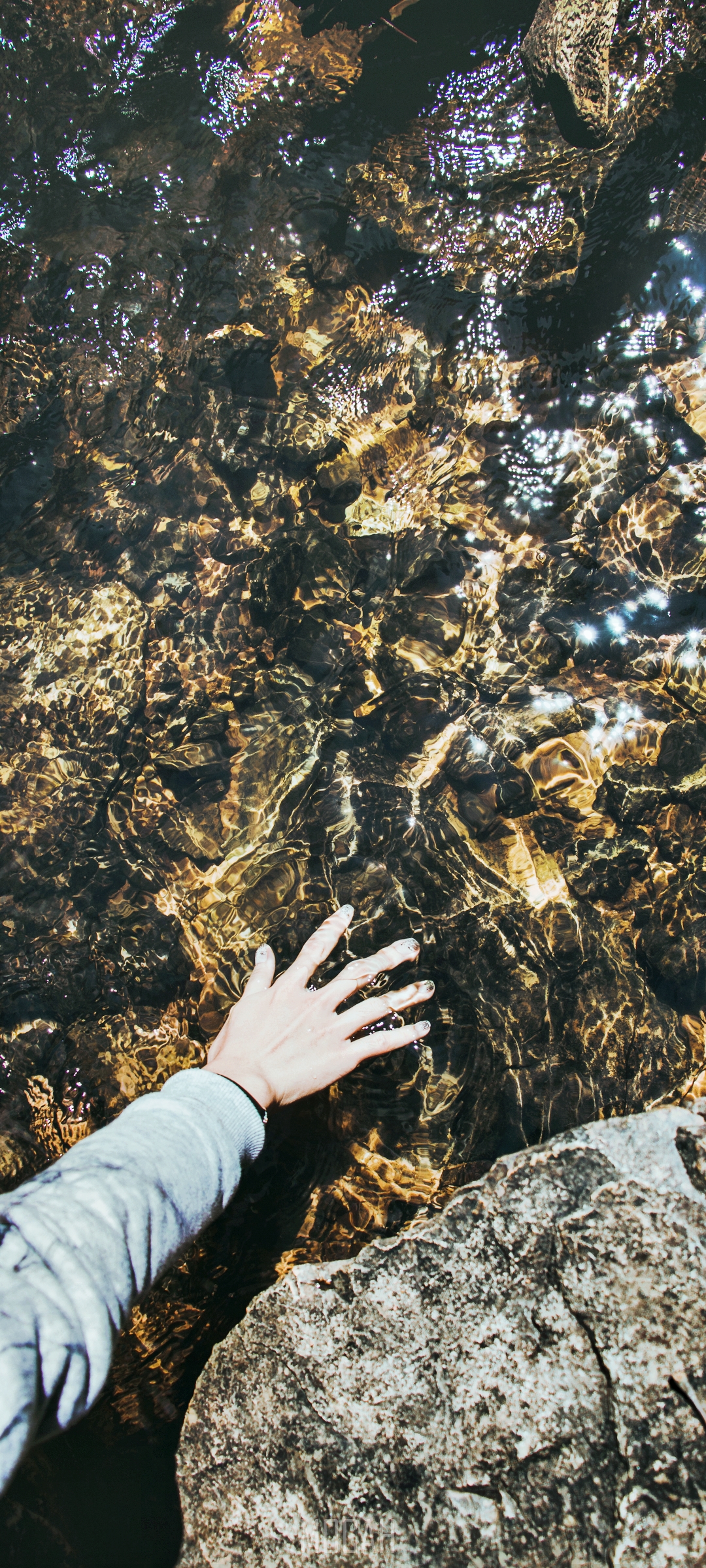 Hand touching clear water over rocks HD Phone Wallpaper
