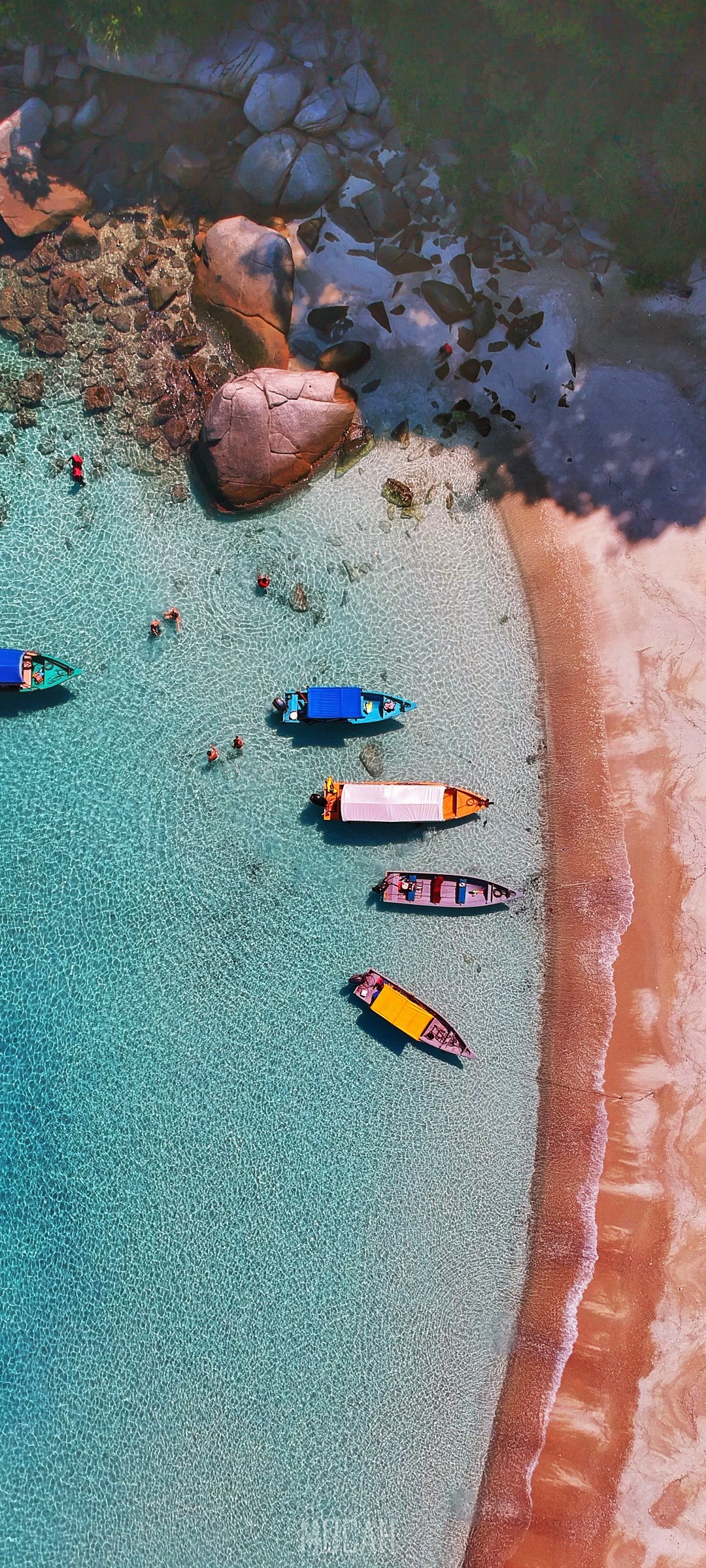 Aerial view of boats and people swimming in clear turquoise water near a sandy beach with large rocks. HD Phone Wallpaper