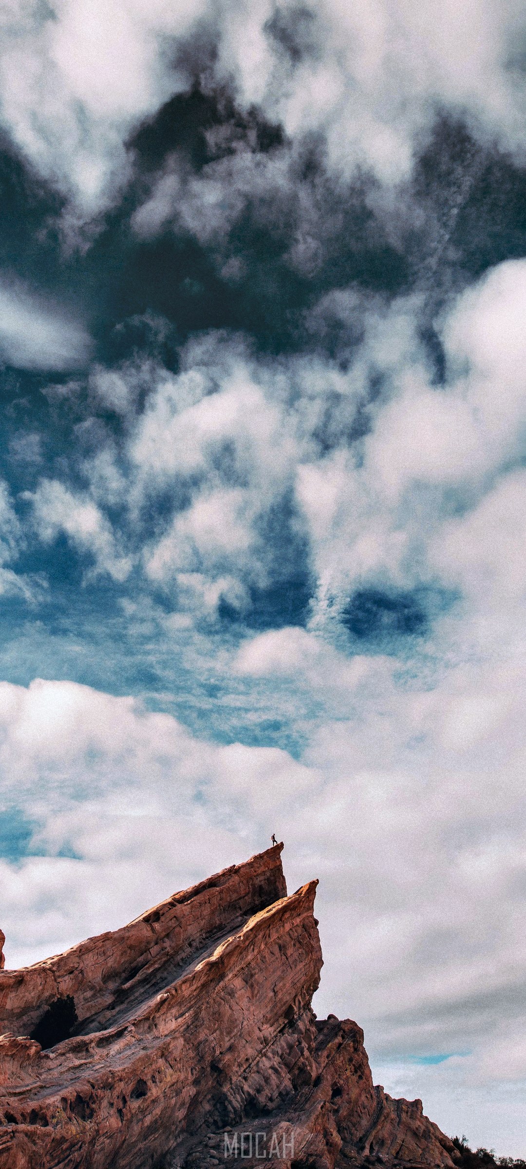 Hiker on a rock ledge under a cloudy sky HD Phone Wallpaper