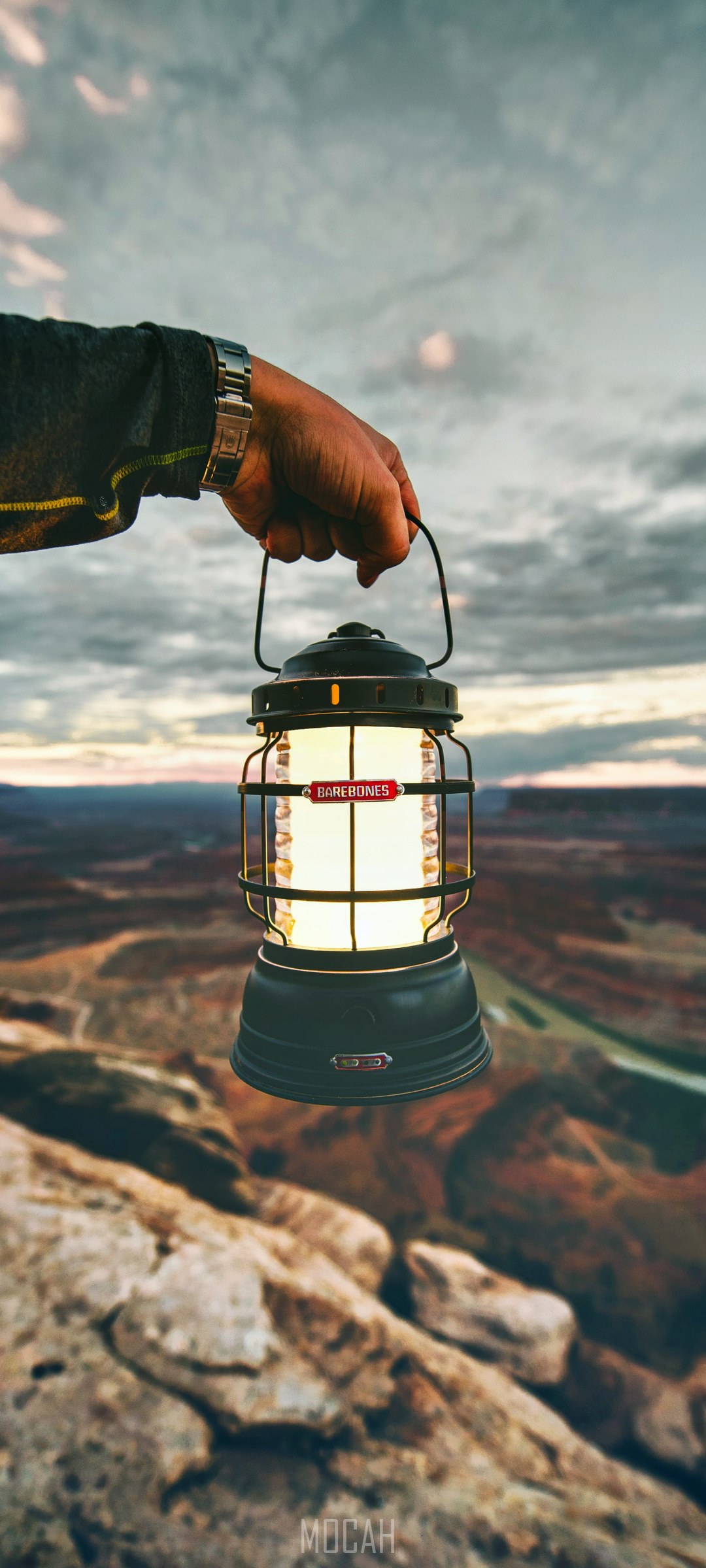 Hand holding Barebones lantern over canyon landscape HD Phone Wallpaper