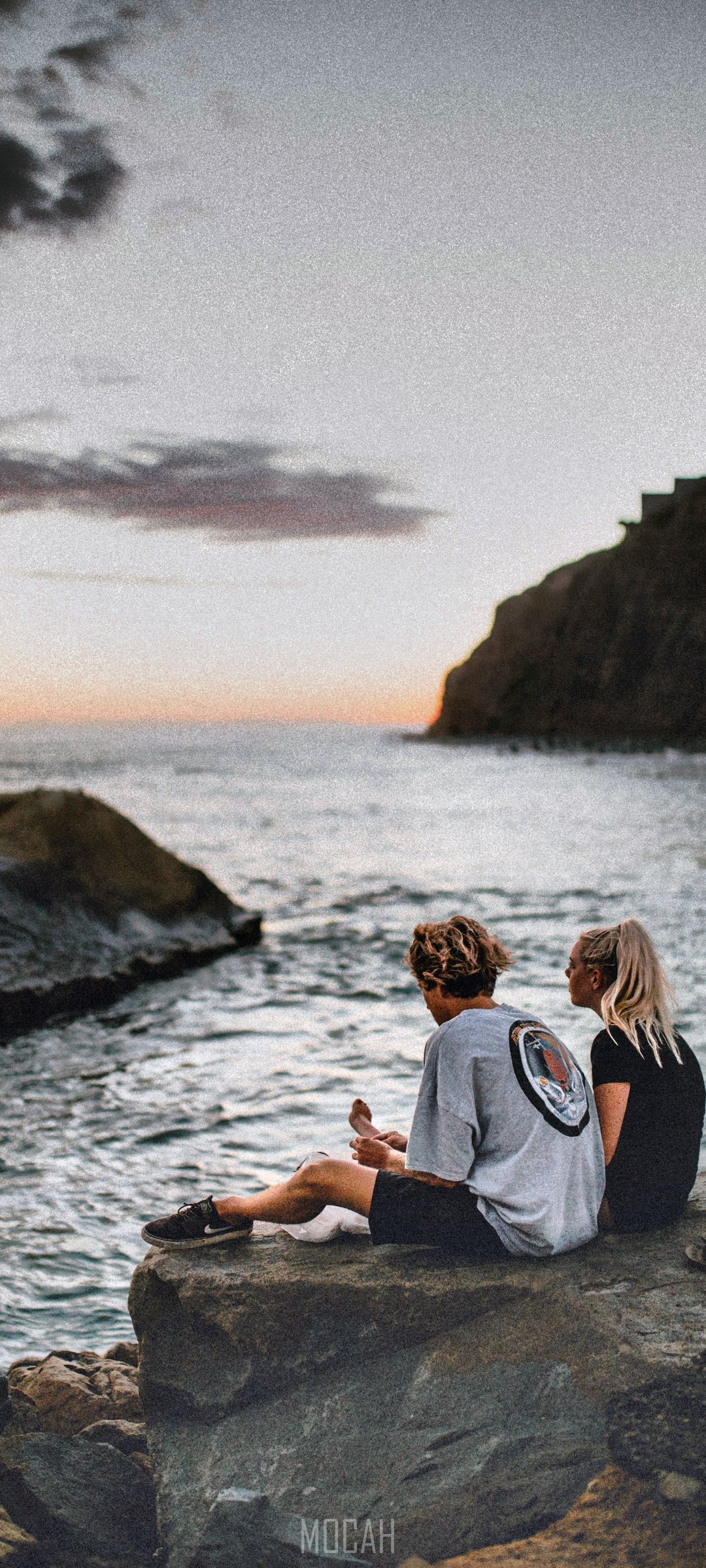 Couple sitting on rocks by the ocean at sunset HD Phone Wallpaper