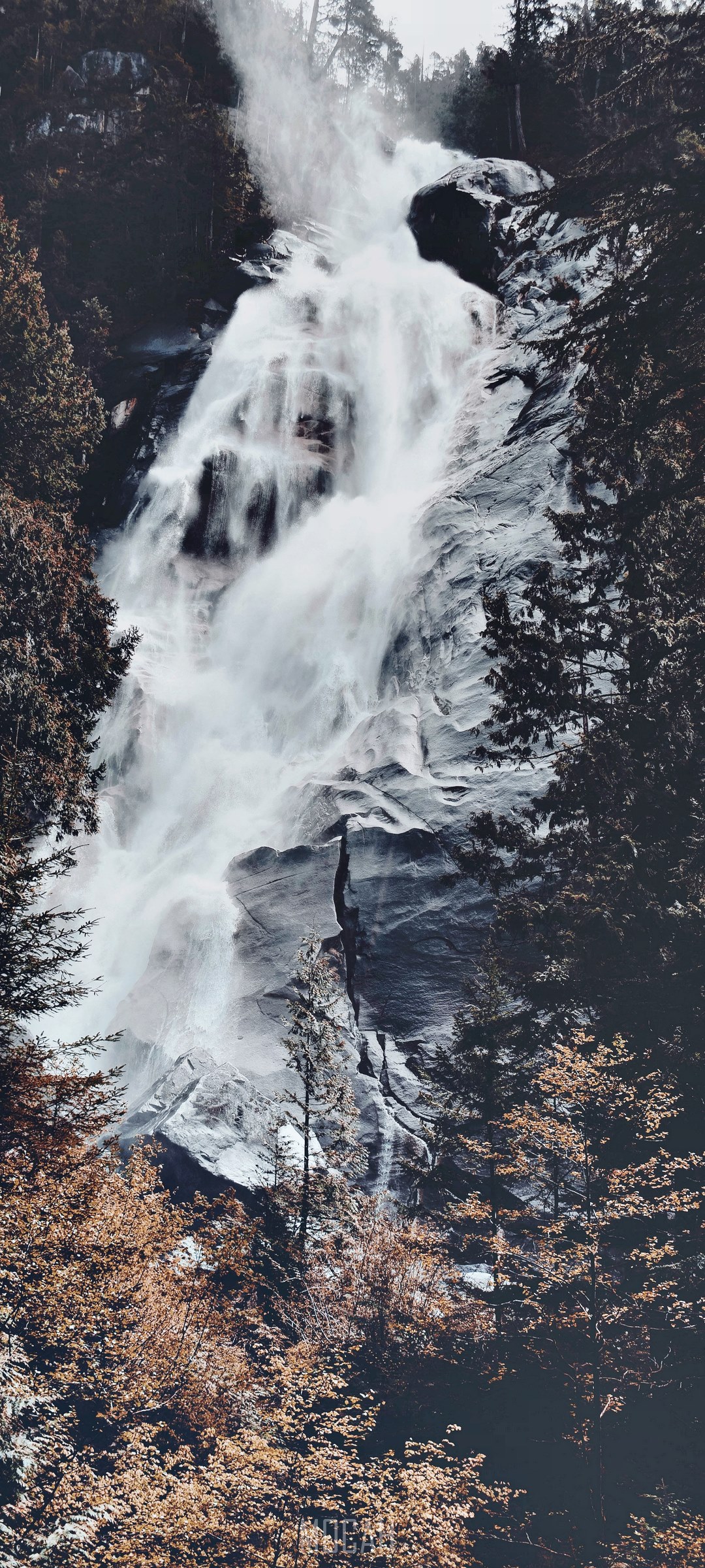 Waterfall cascading down a rocky cliff face surrounded by trees HD Phone Wallpaper