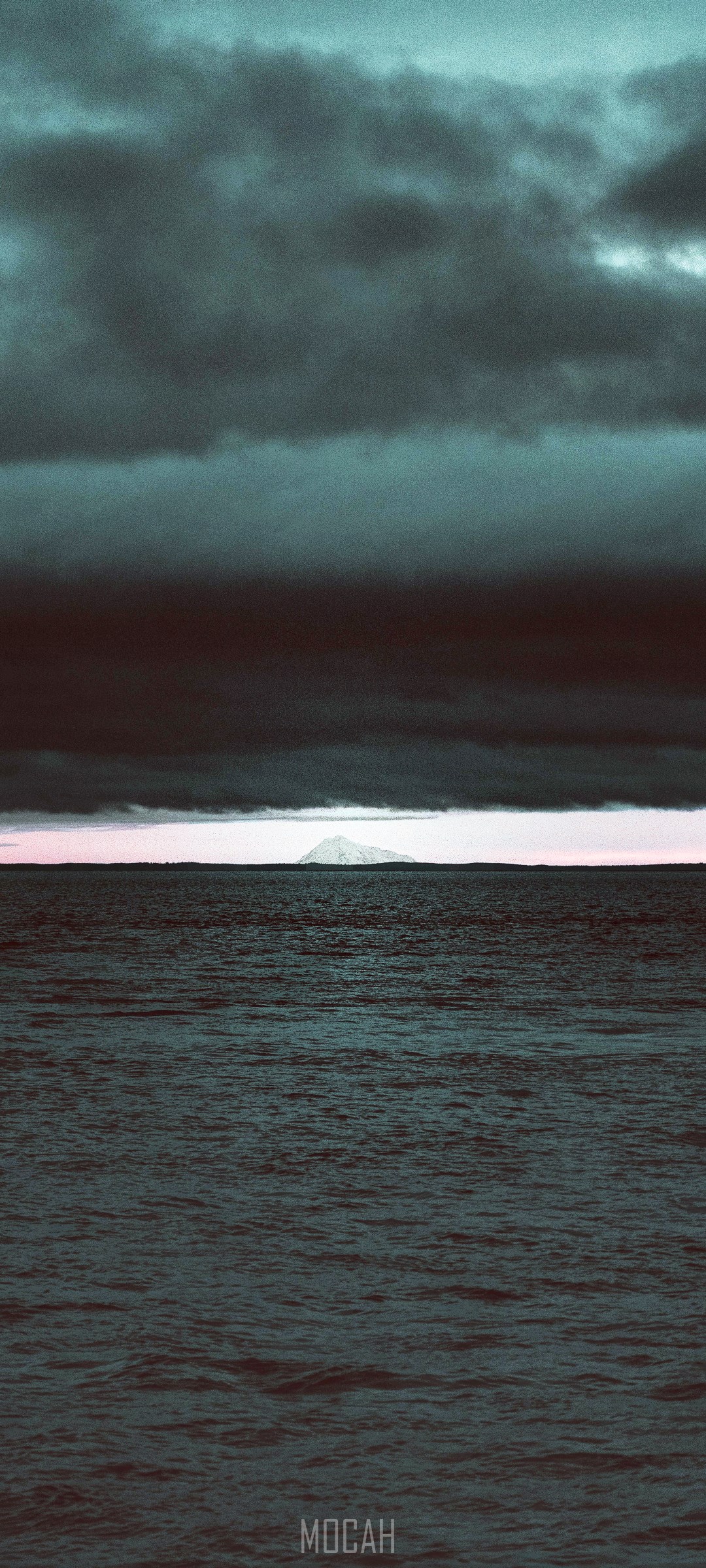 Mountain island on the horizon over the sea under dark clouds HD Phone Wallpaper