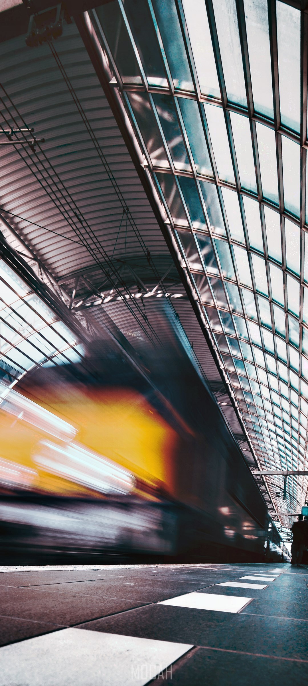 Train speeding through a modern train station with glass roof HD Phone Wallpaper