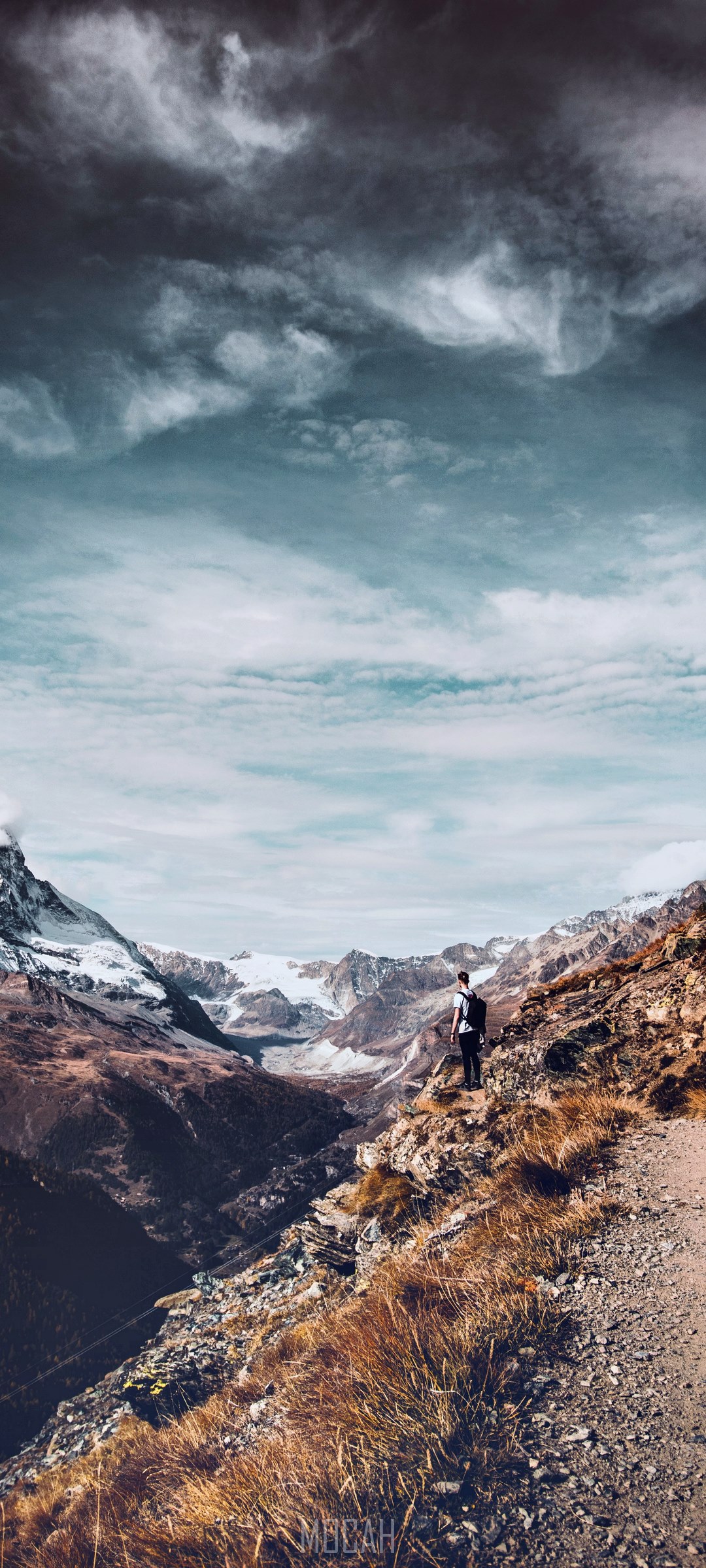 Man on mountain path overlooking snowy peaks HD Phone Wallpaper