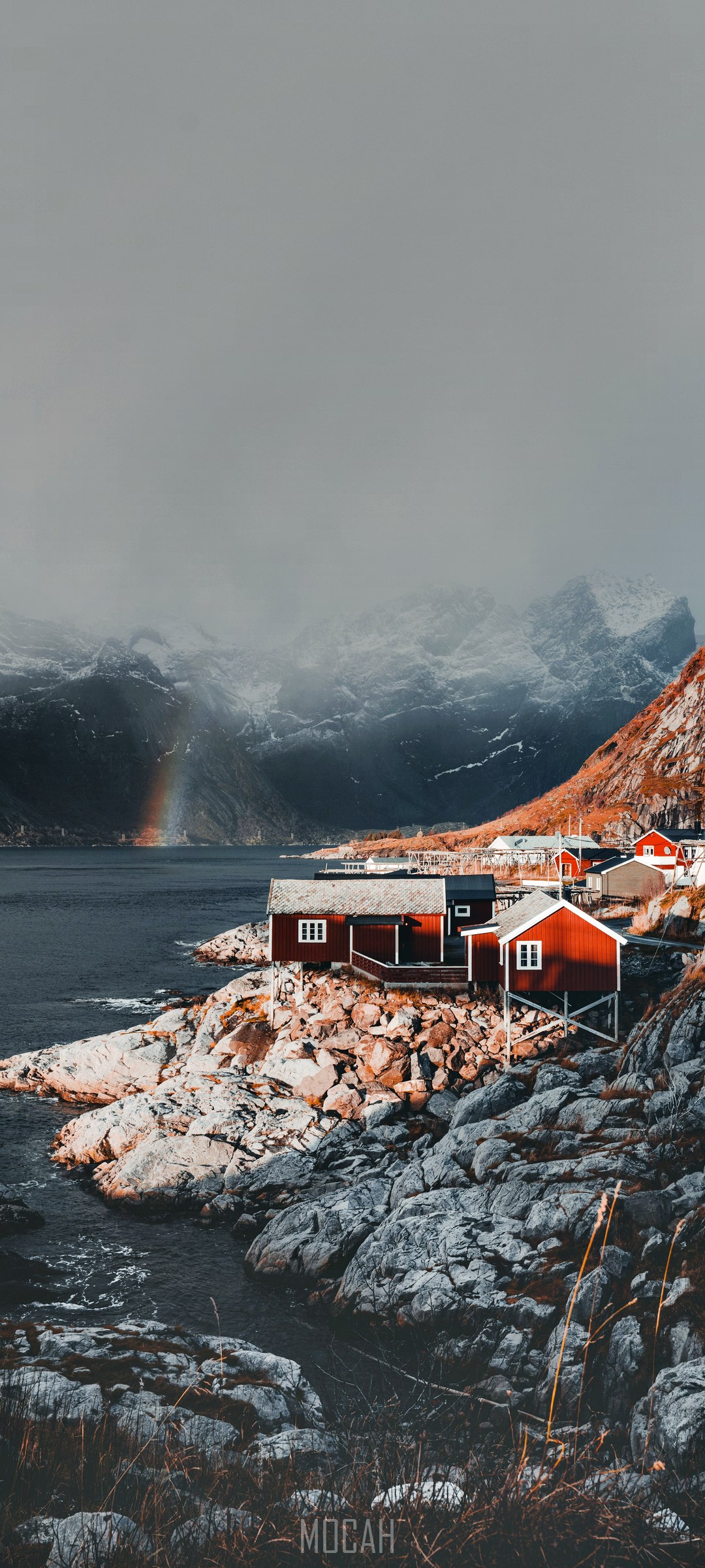 Red cabins on a rocky coast with mountains and a rainbow HD Phone Wallpaper