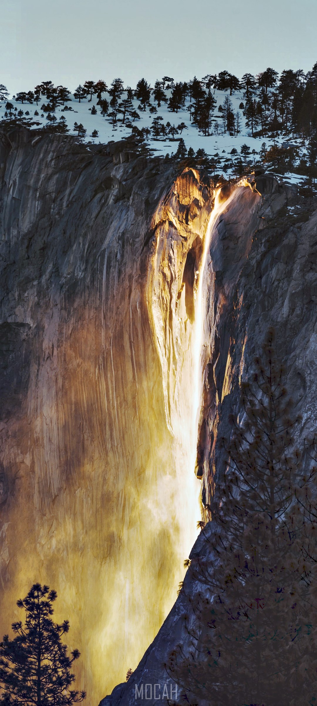 Waterfall illuminated by sunset on a rocky cliff with snow and trees HD Phone Wallpaper