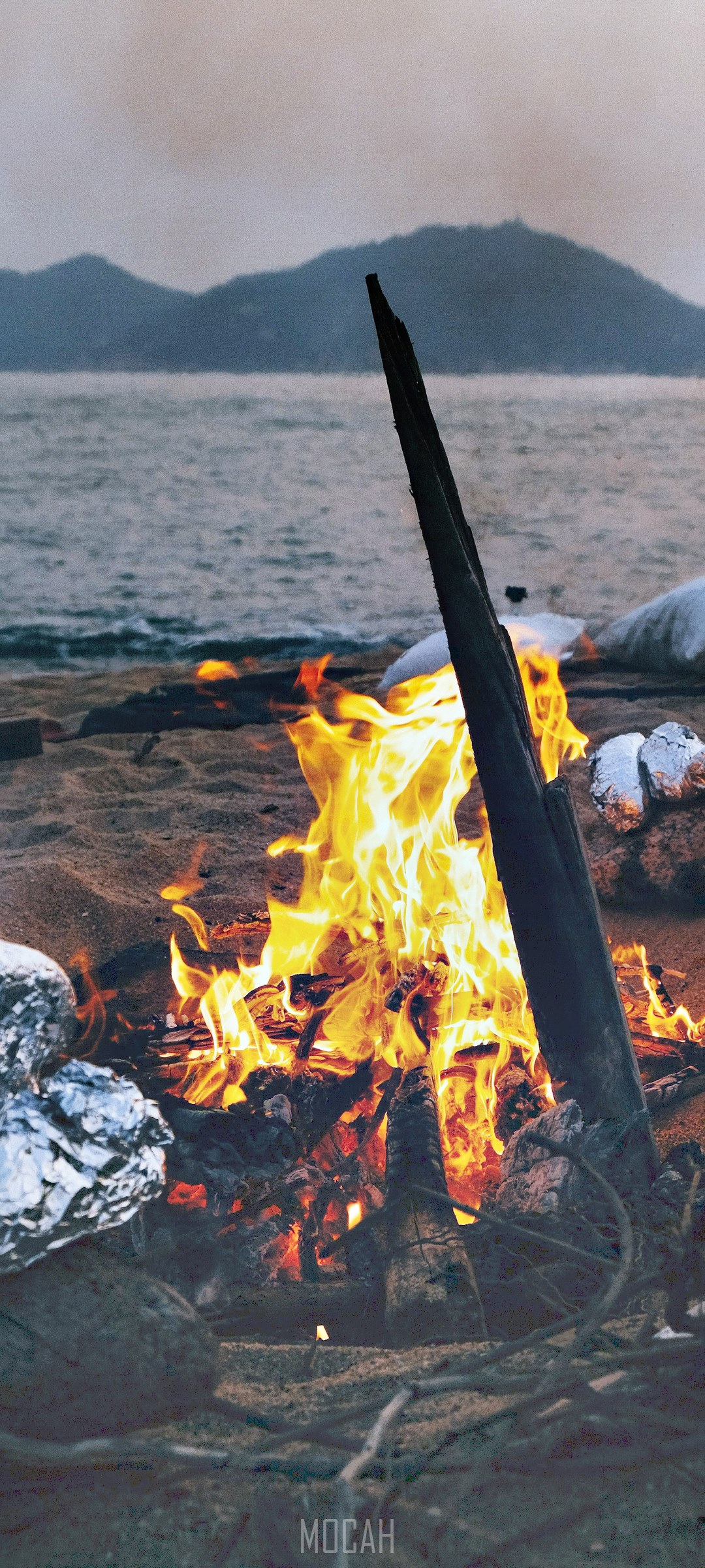 Campfire on a beach with mountains in the background HD Phone Wallpaper