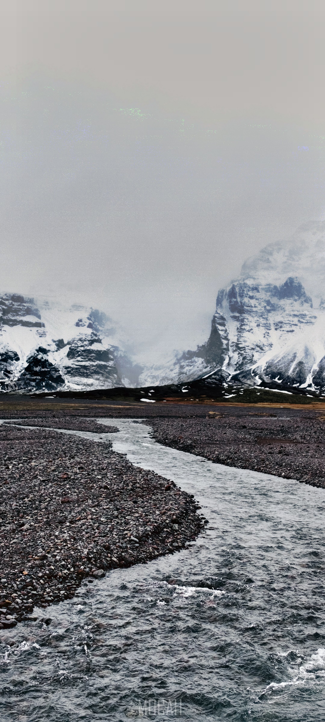 River flowing through a rocky plain towards snow-capped mountains HD Phone Wallpaper