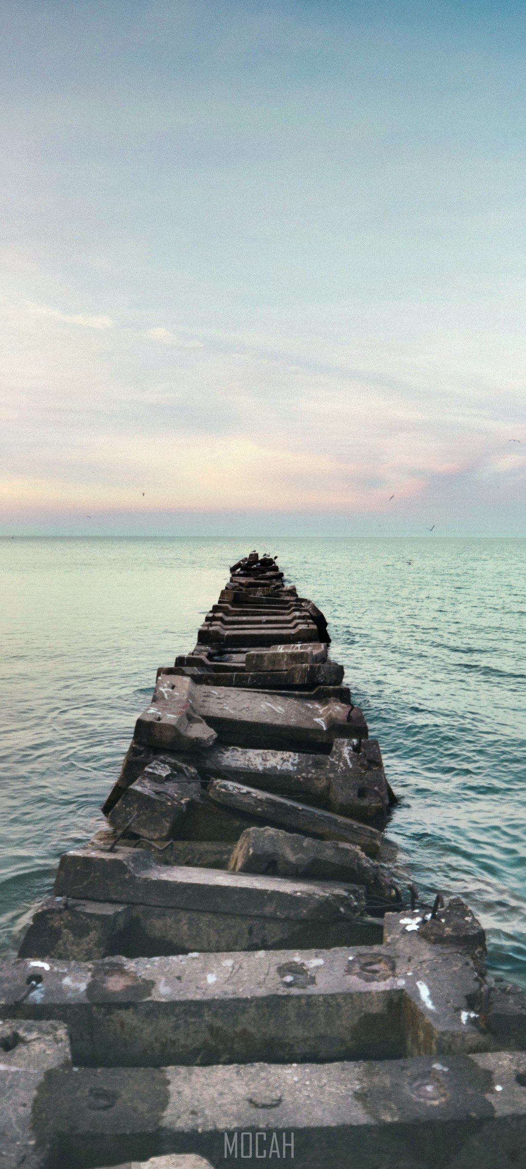 Stone pier extending into the ocean at sunset HD Phone Wallpaper
