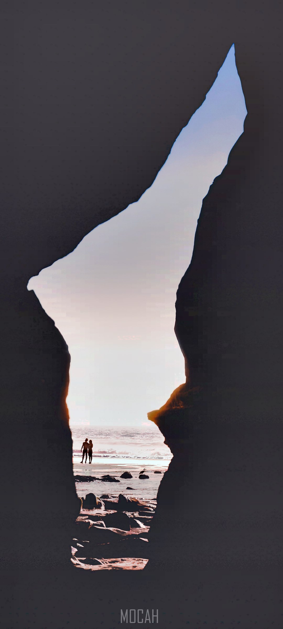 Couple silhouetted against the ocean through rock archway HD Phone Wallpaper