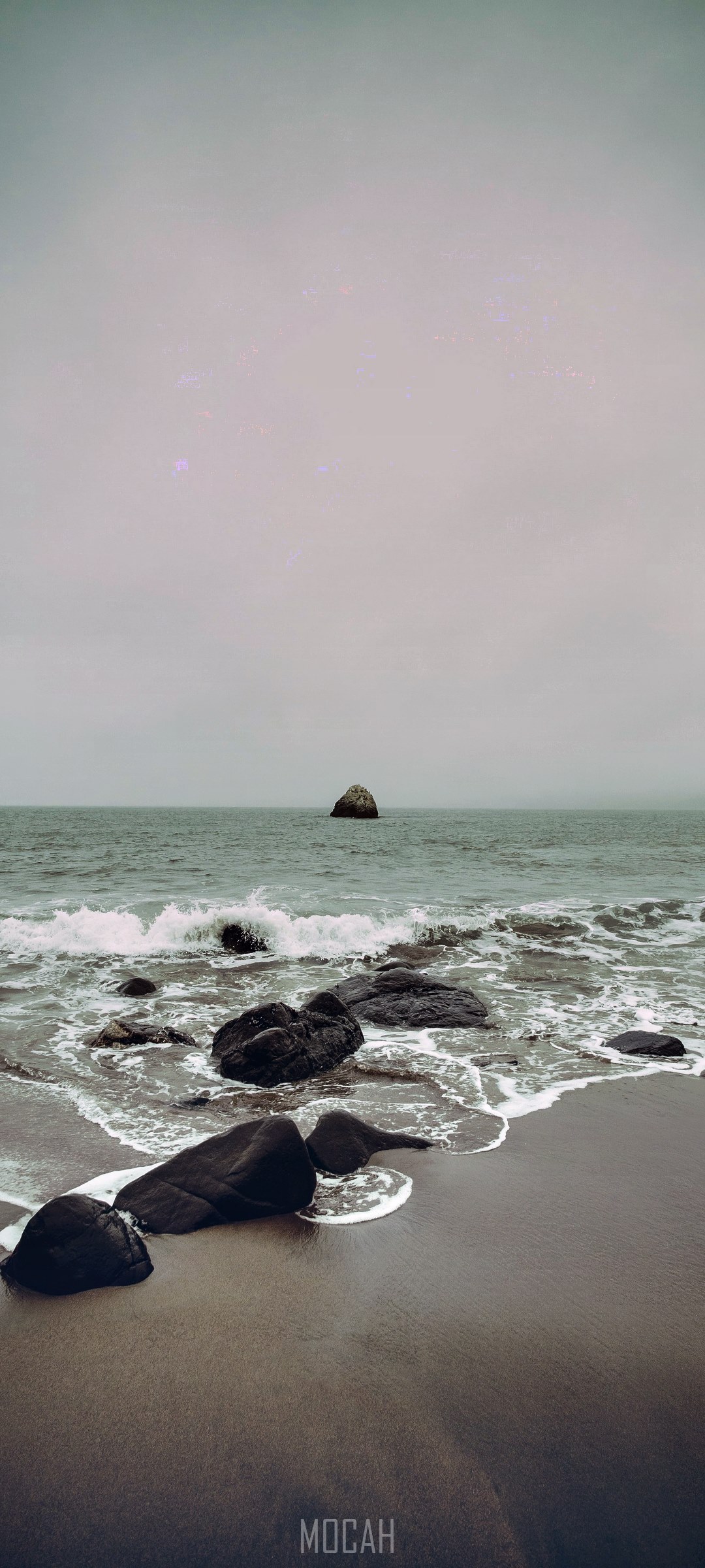Rocks on a beach with waves and a distant rock formation HD Phone Wallpaper