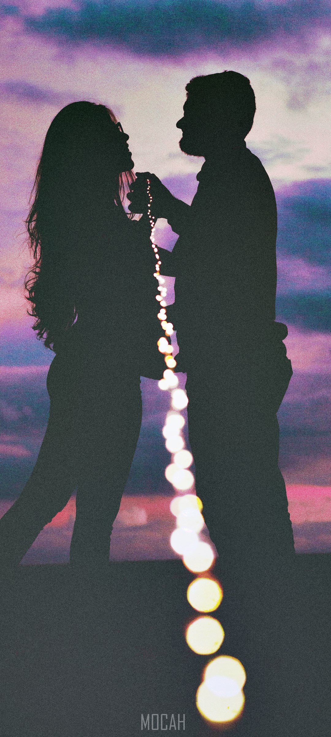 Couple silhouetted against a colorful sunset with bokeh lights HD Phone Wallpaper