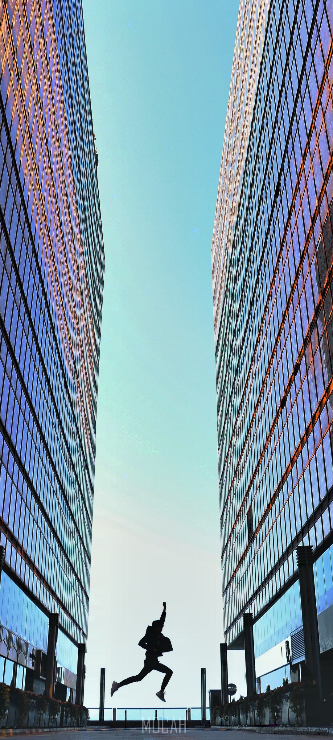 Silhouette of a person jumping between two modern buildings HD Phone Wallpaper