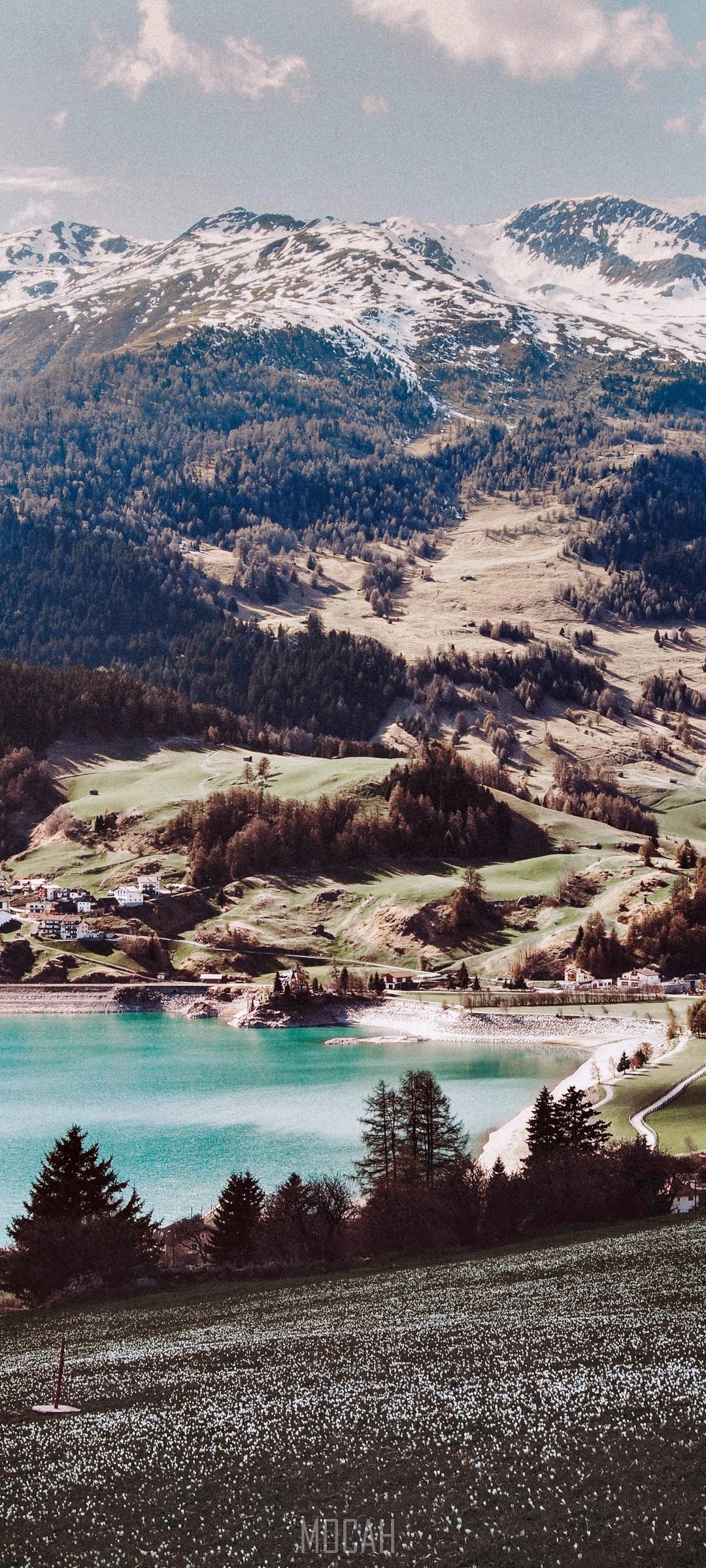 Snow-capped mountains overlooking a turquoise lake and village HD Phone Wallpaper