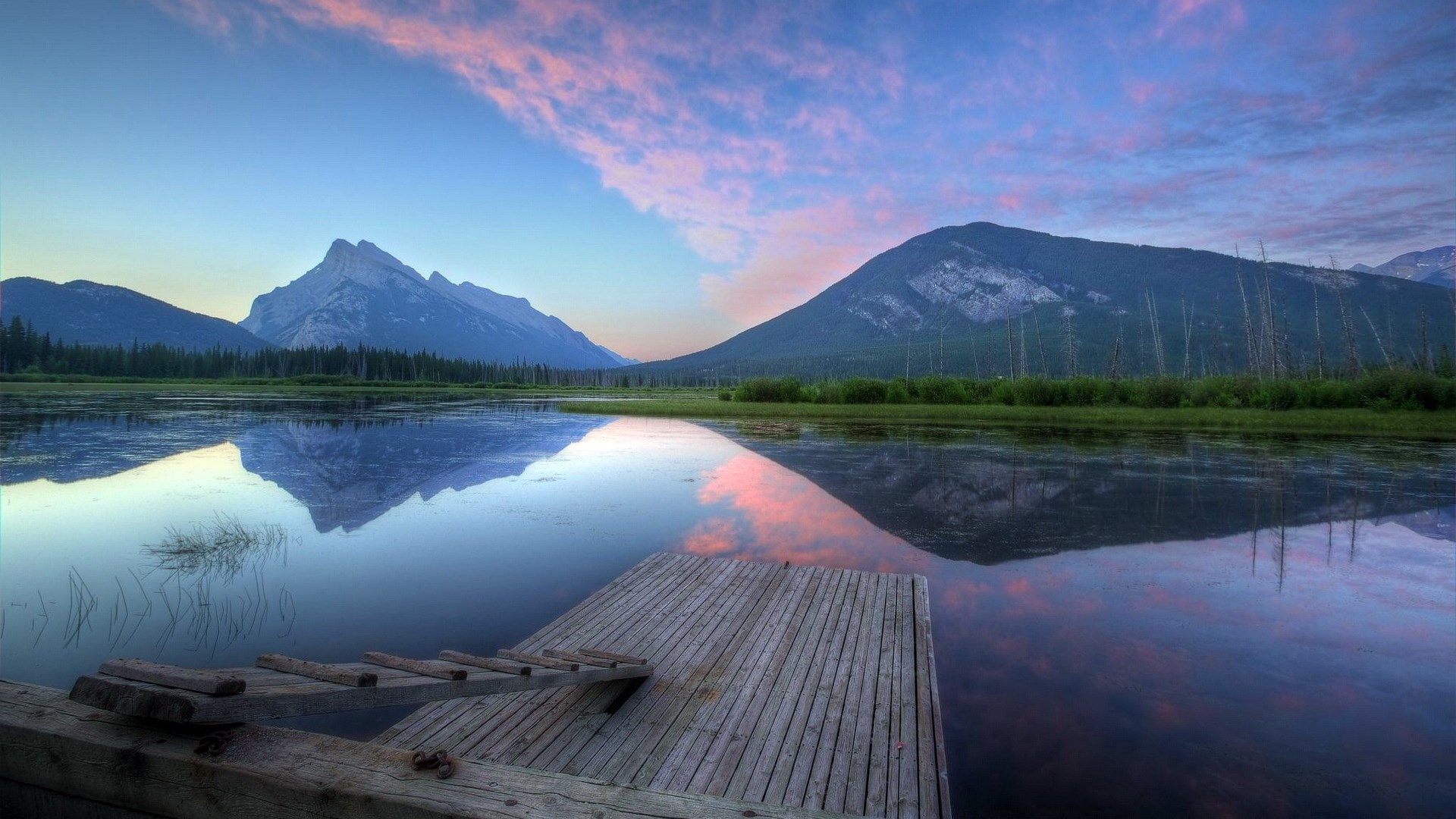 Wooden dock on a calm lake with mountains and colorful sky reflection HD Wallpaper