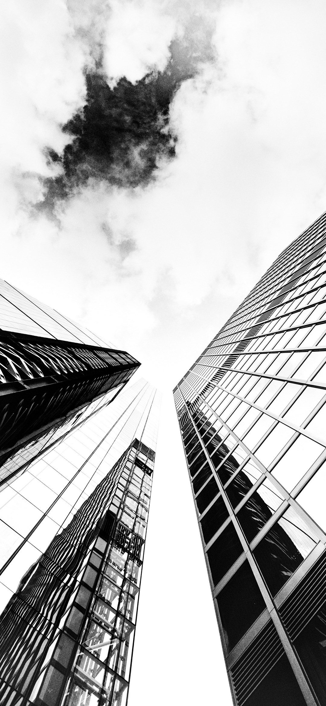 a low angle monochrome shot of glass skyscraper facades under cloudy ...