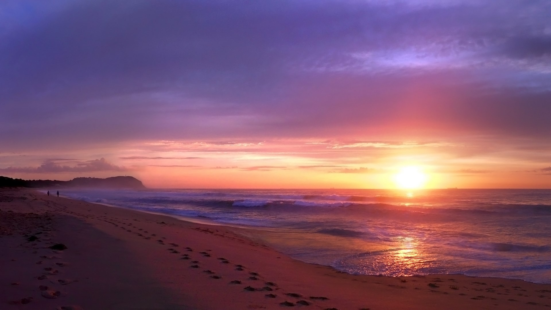 Sunset over a beach with footprints HD Wallpaper