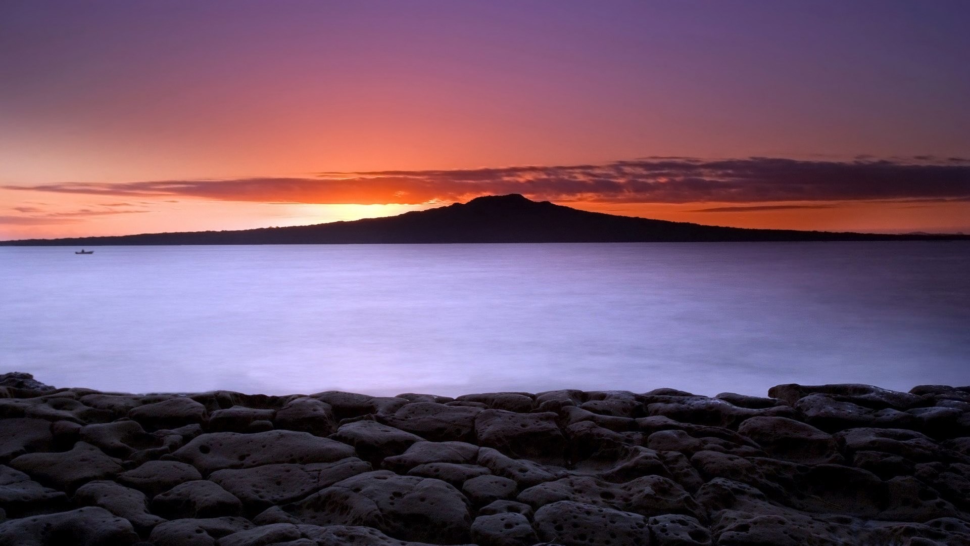 Volcanic island silhouette at sunset over the ocean HD Wallpaper