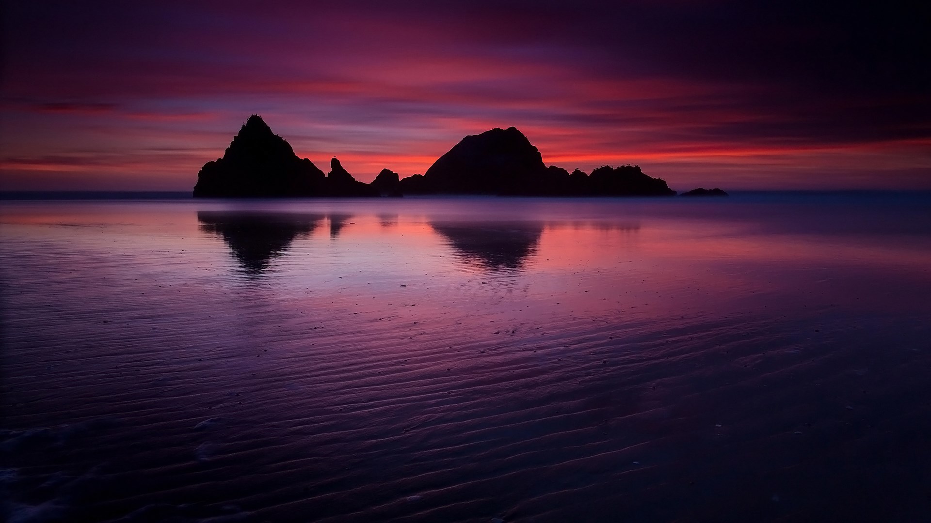 Silhouette of rock formations on a beach at sunset HD Wallpaper