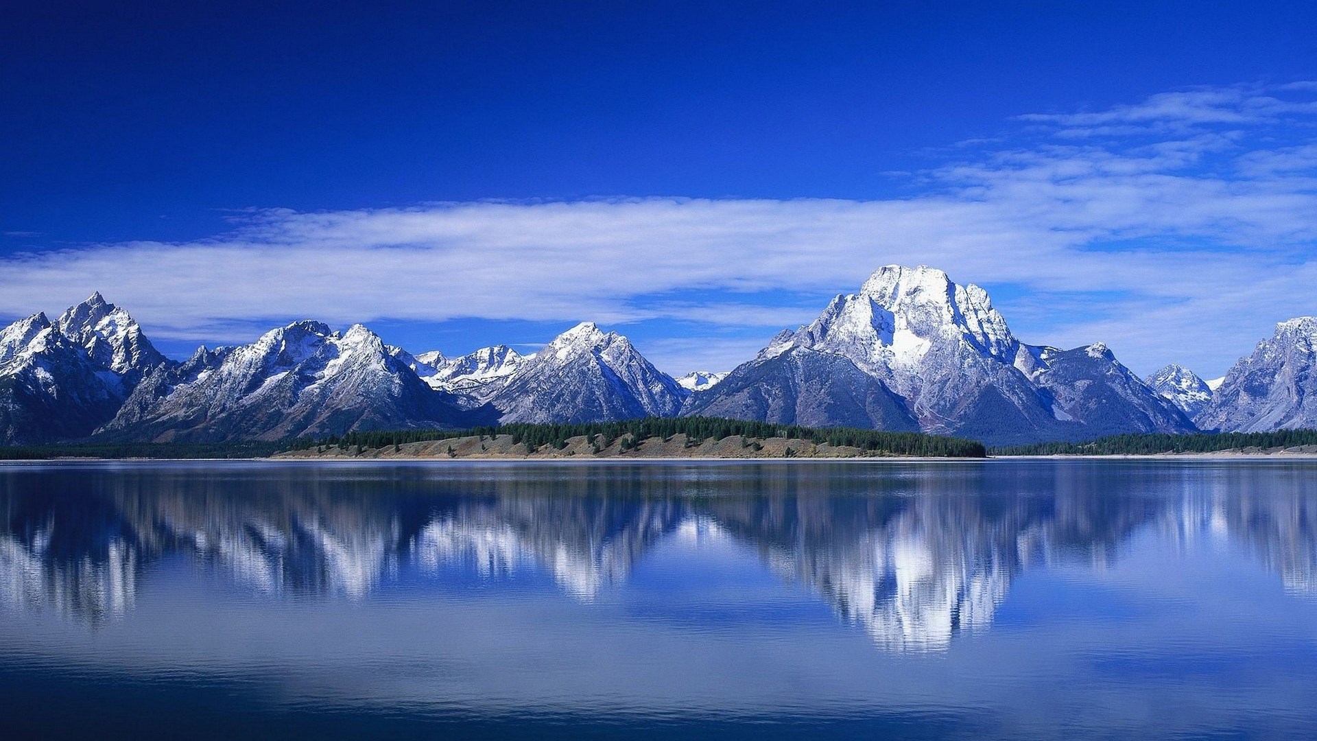Snow-capped mountains reflected in a calm lake under a blue sky HD Wallpaper