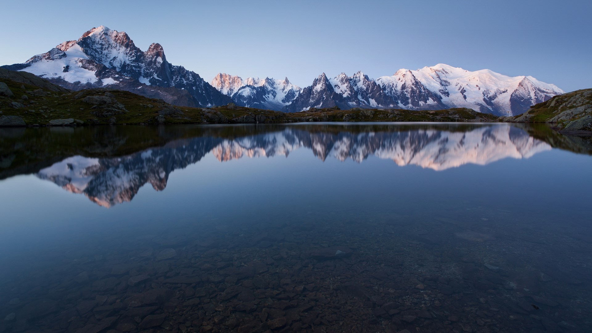 Snow-capped mountains reflected in a calm lake at sunrise HD Wallpaper