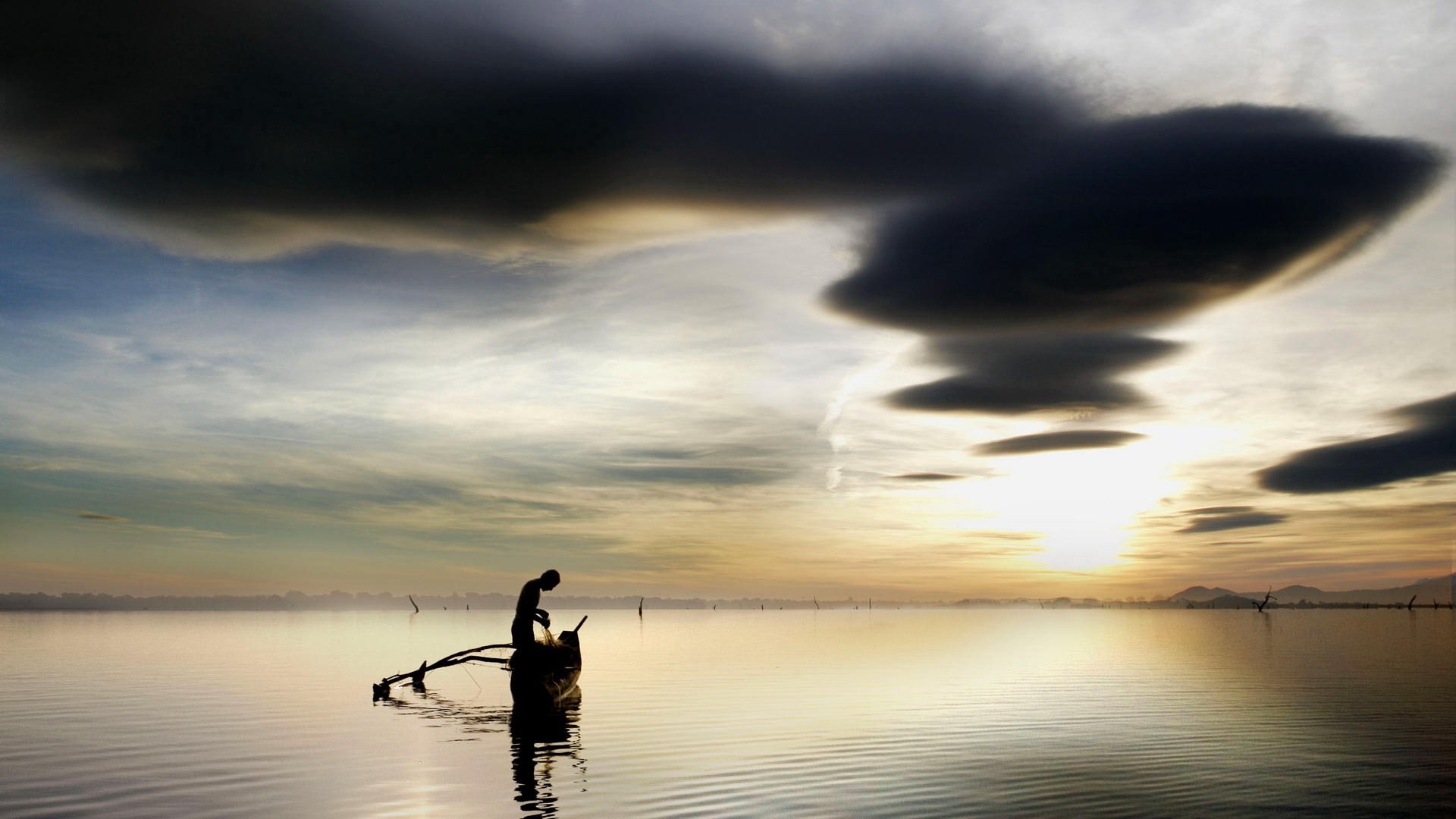 Fisherman in a boat at sunrise with dark clouds HD Wallpaper