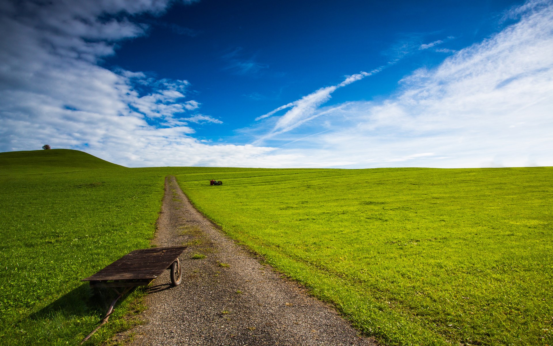 Dirt path through a green field with a cart and a tractor HD Wallpaper