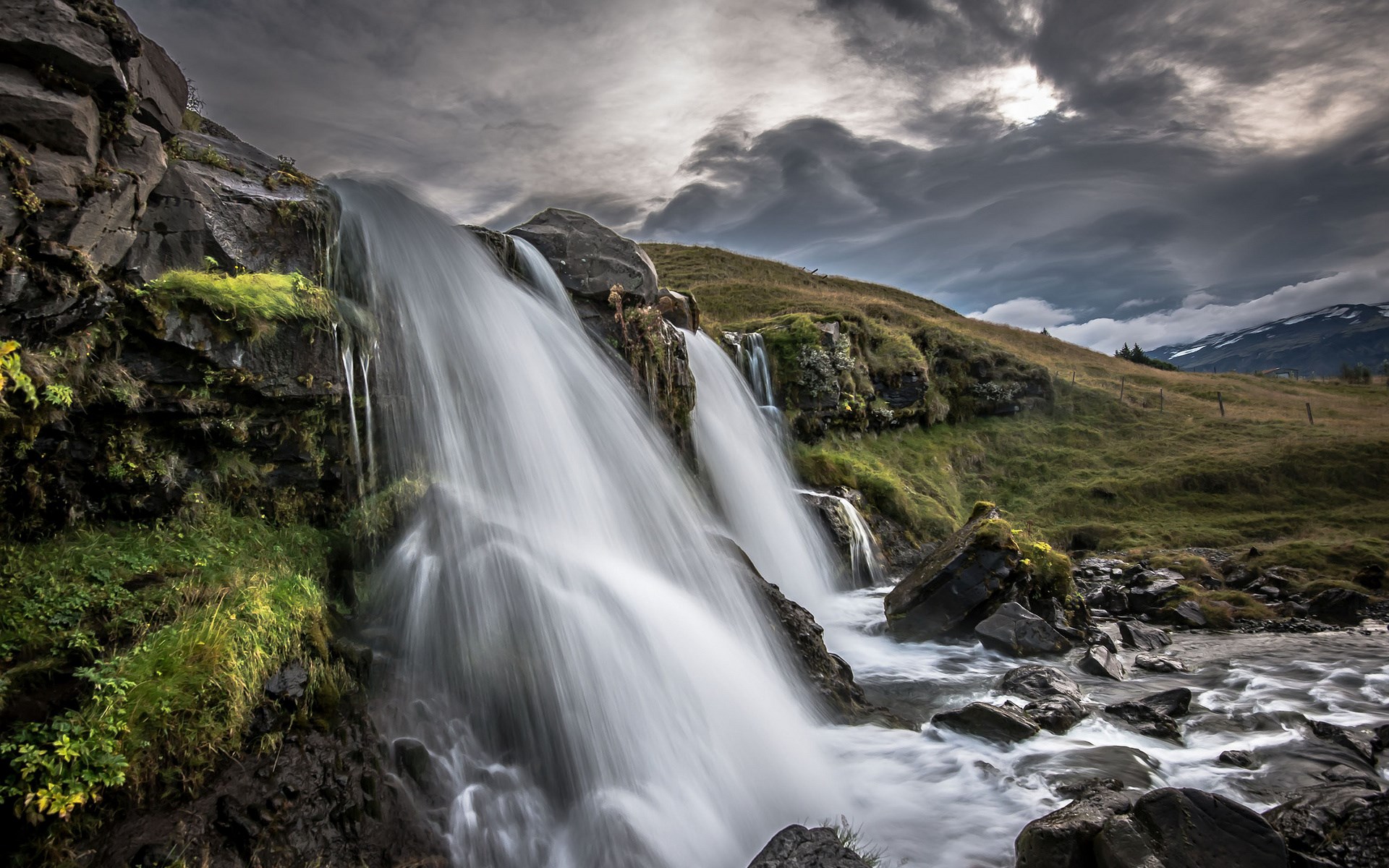 Waterfall cascading over rocks with stormy sky HD Wallpaper