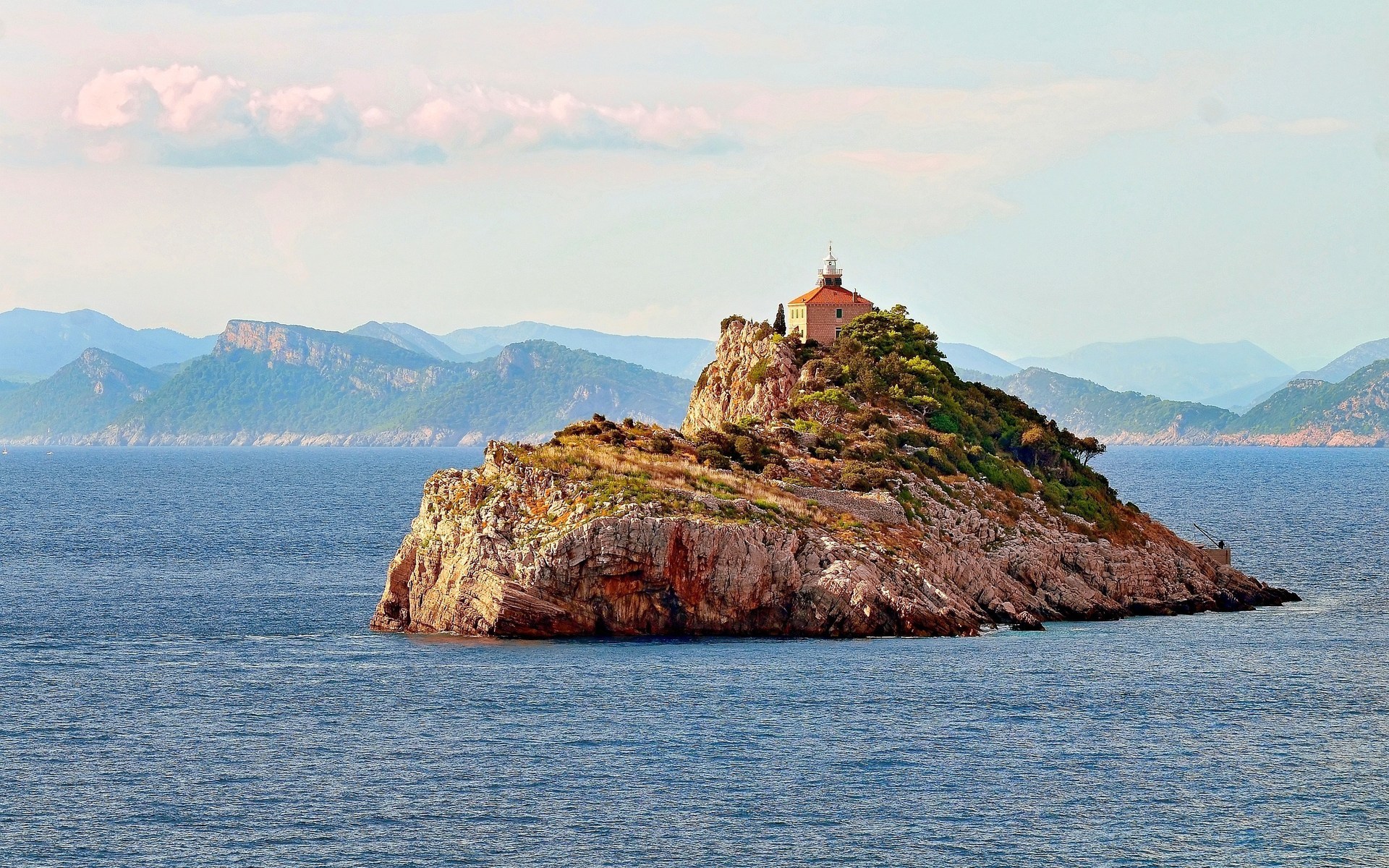 Island with lighthouse and mountains in the background HD Wallpaper