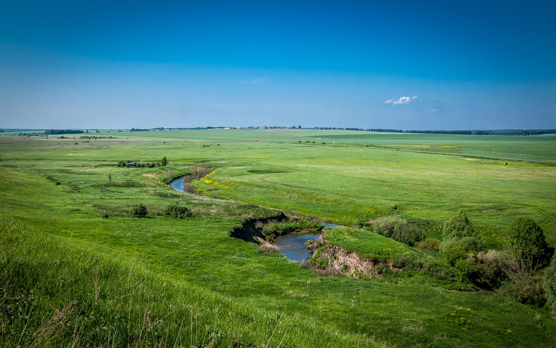 A winding river through green fields under a blue sky HD Wallpaper