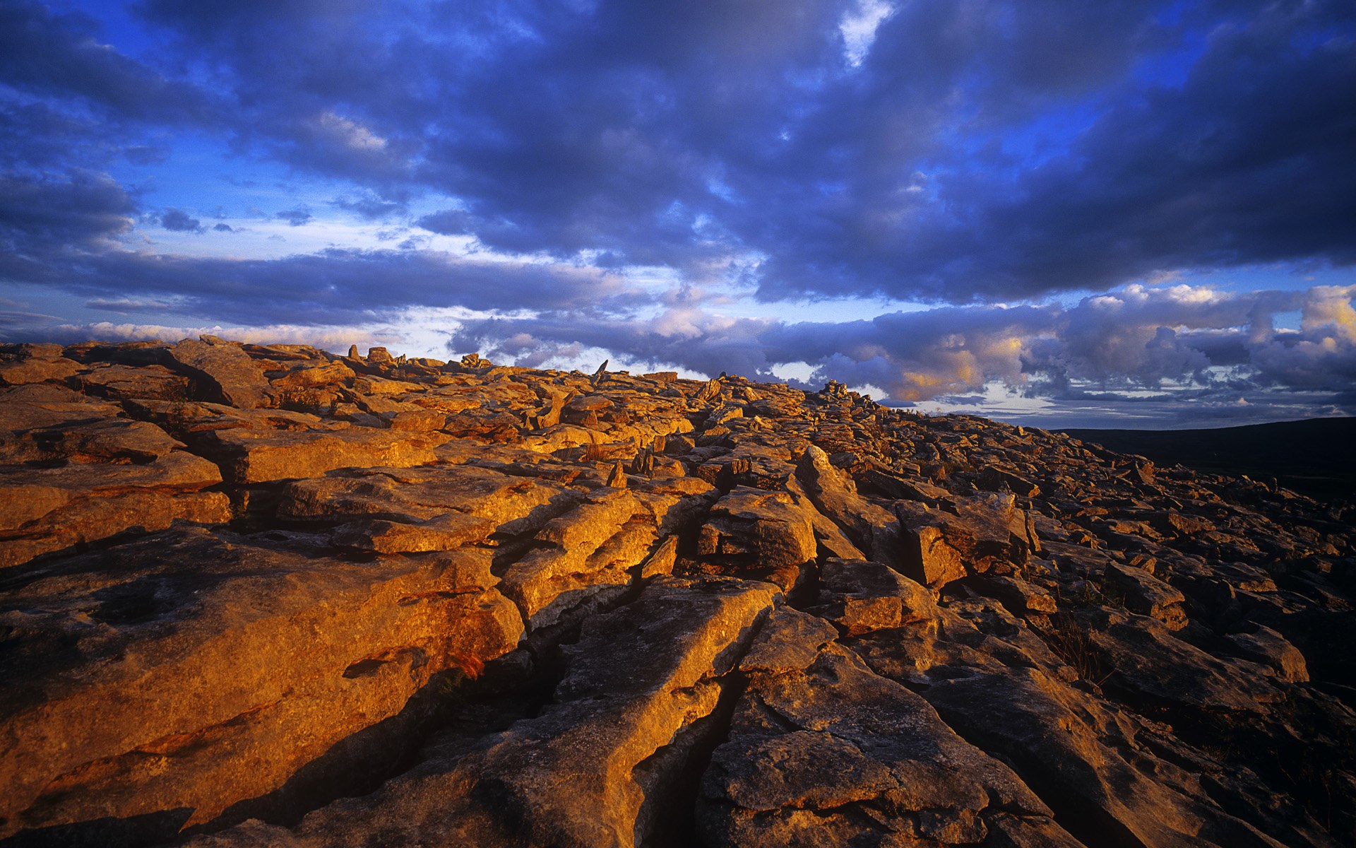 Rocky terrain under a dramatic cloudy sky HD Wallpaper