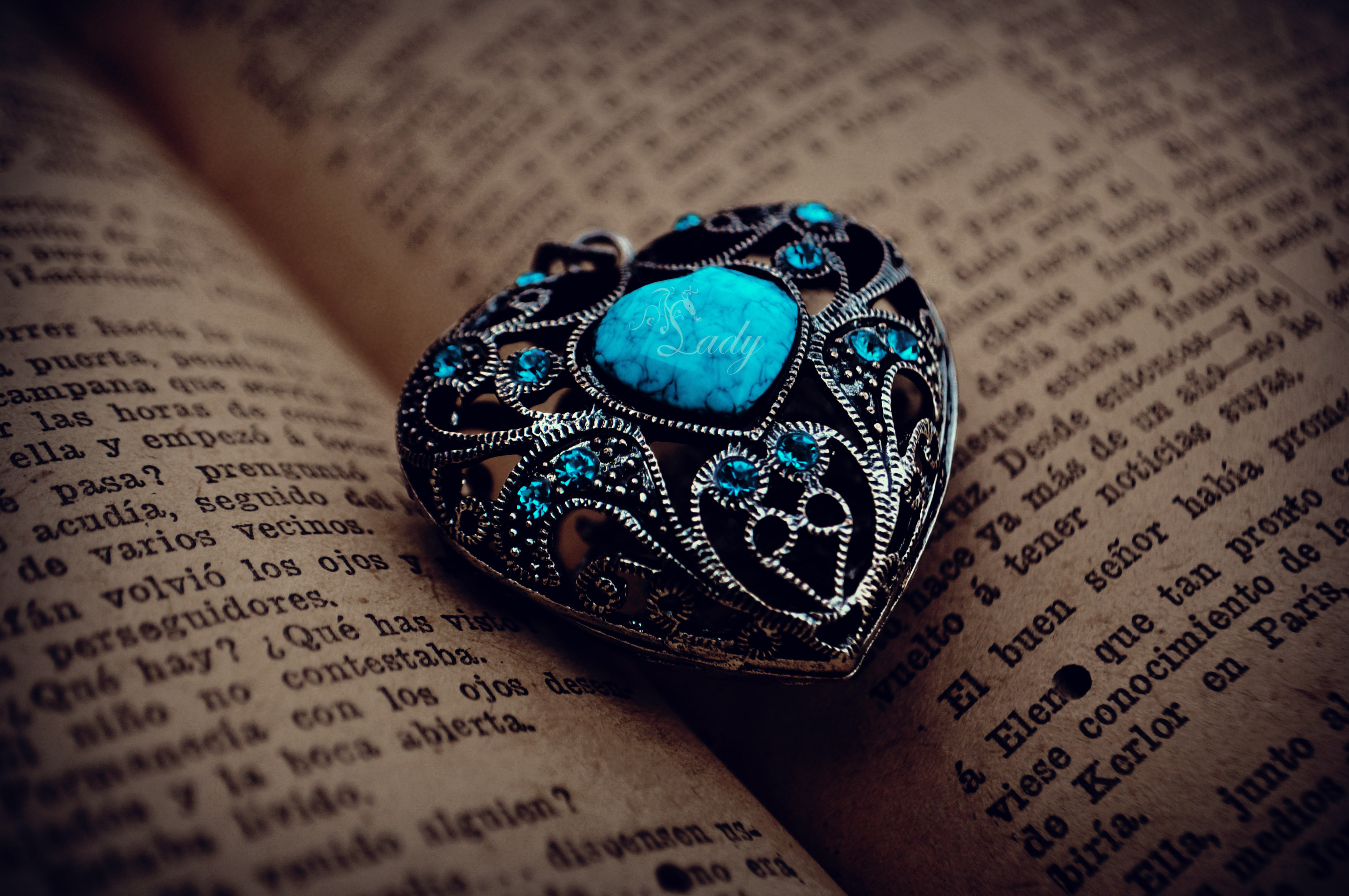 Heart-shaped locket with blue gems on an open book HD Wallpaper