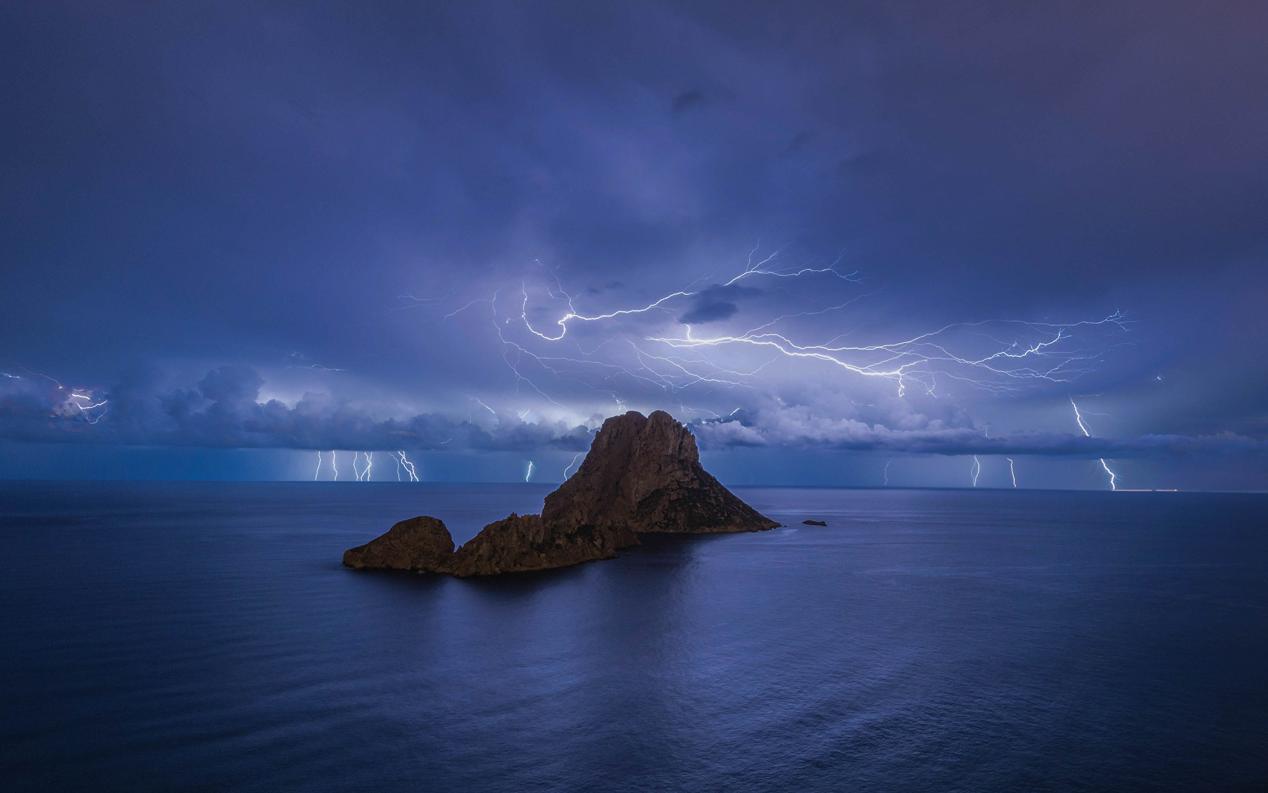 Lightning strikes over a rocky island in the ocean HD Wallpaper