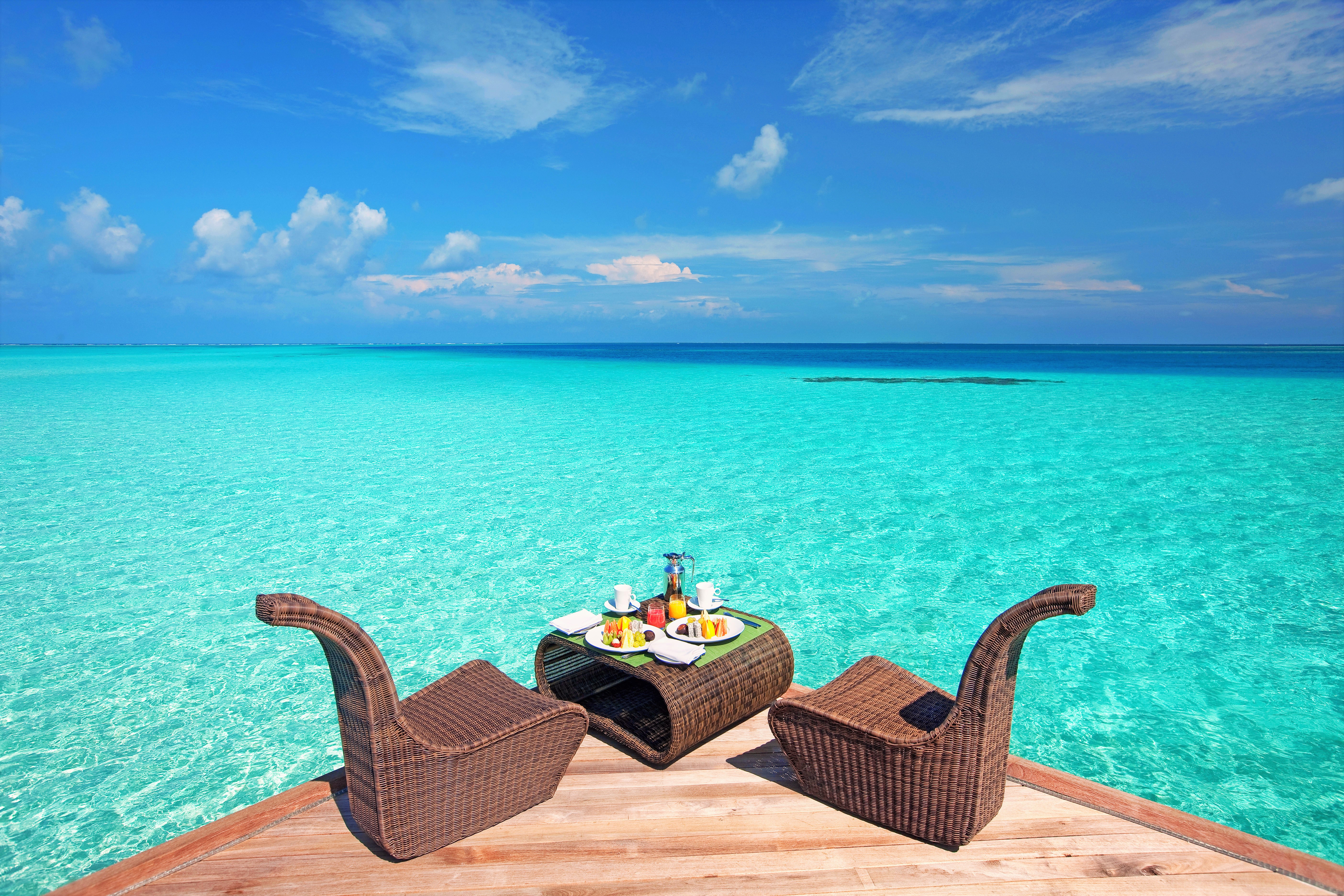 Breakfast table for two on a wooden deck overlooking turquoise ocean HD Wallpaper