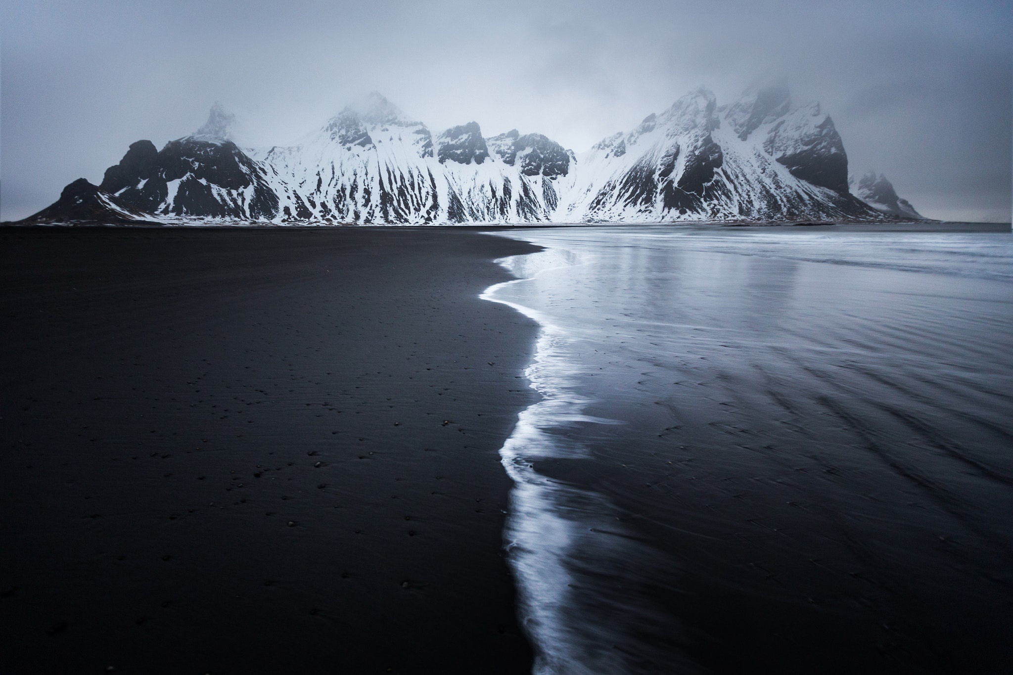 Snow-capped mountains on a black sand beach with fog HD Wallpaper