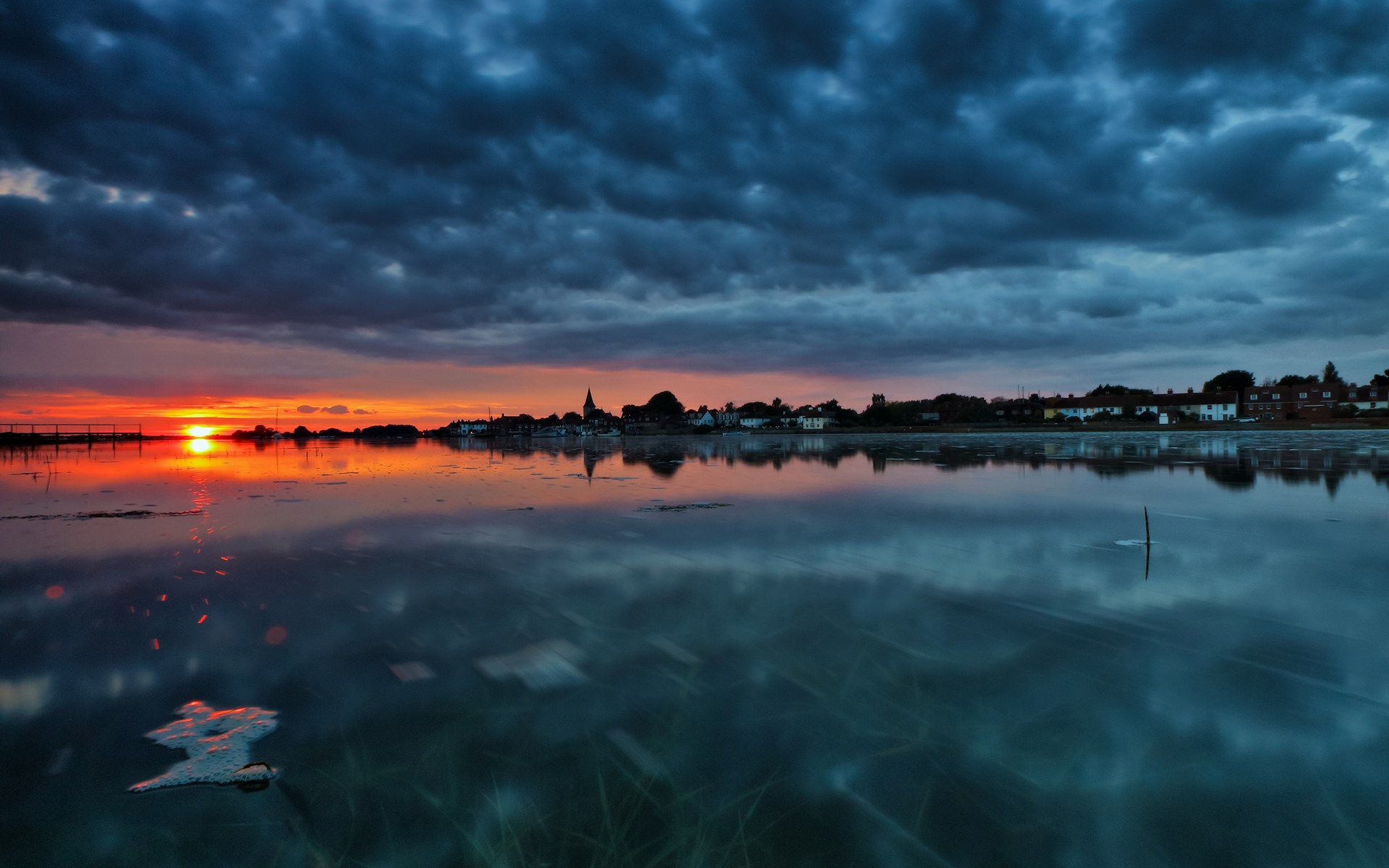 Sunset over a coastal town with dark clouds HD Wallpaper