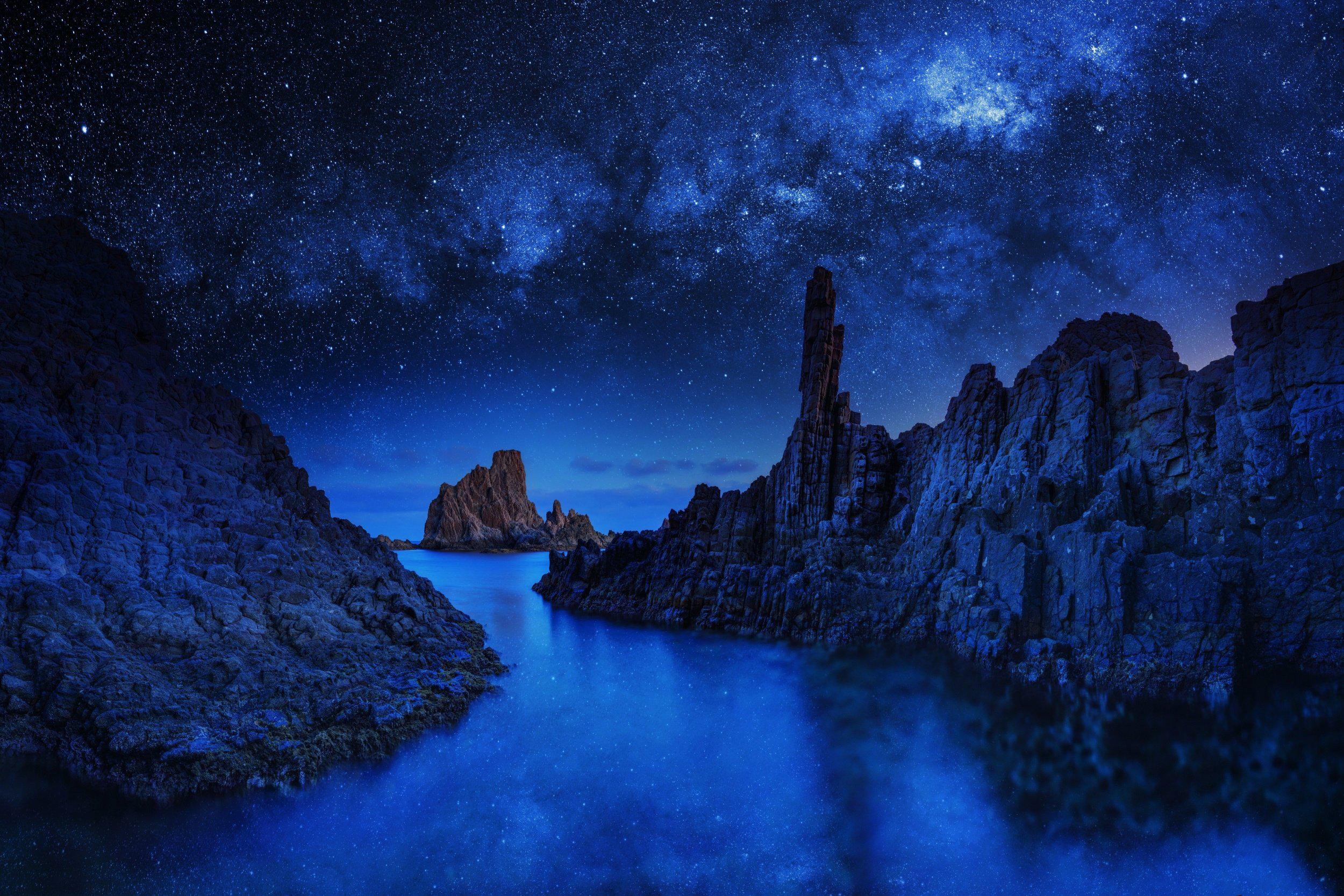 Rocky coast under a starry night sky HD Wallpaper